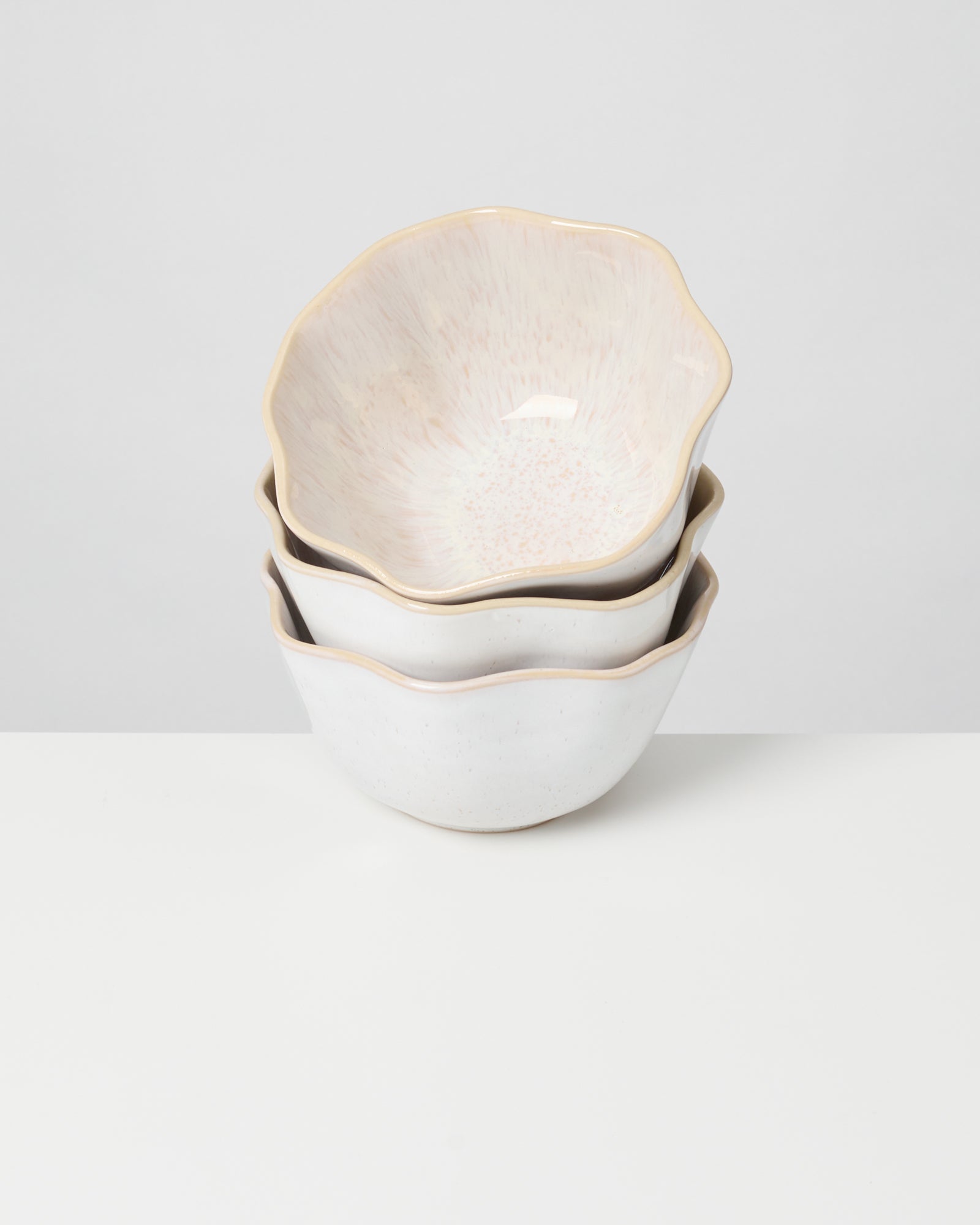 Drei gestapelte weiß-beige Schalen mit gewelltem Rand auf einem weißen Hintergrund.