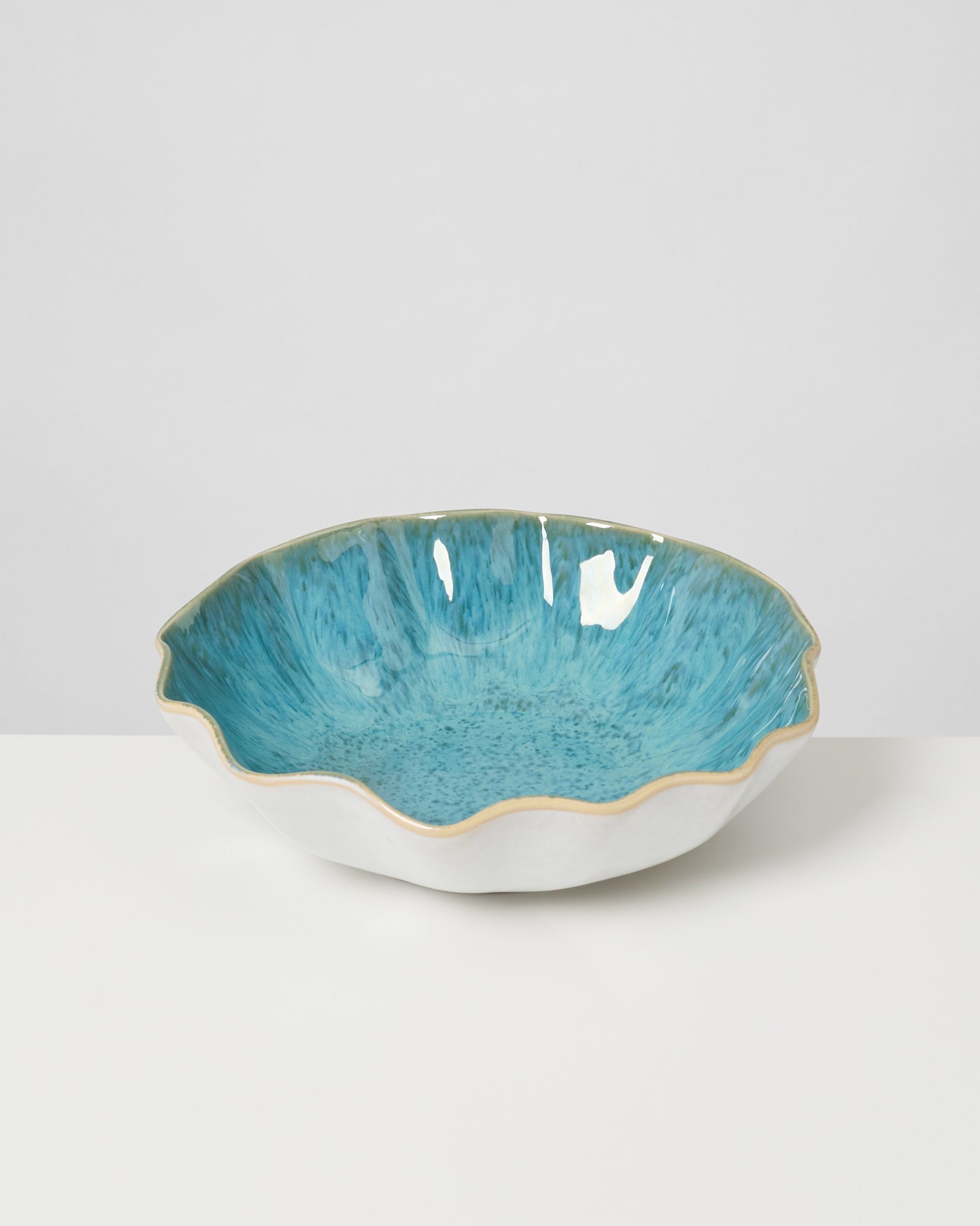 Keramikschale mit gewelltem Rand, außen weiß und innen türkis, steht auf einer weißen Oberfläche.