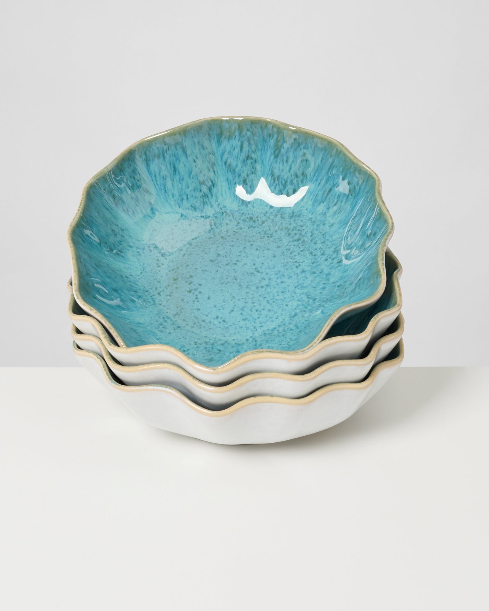 Ein Stapel von vier blau-grünen, wellenförmigen Keramikschalen steht auf einem weißen Untergrund.