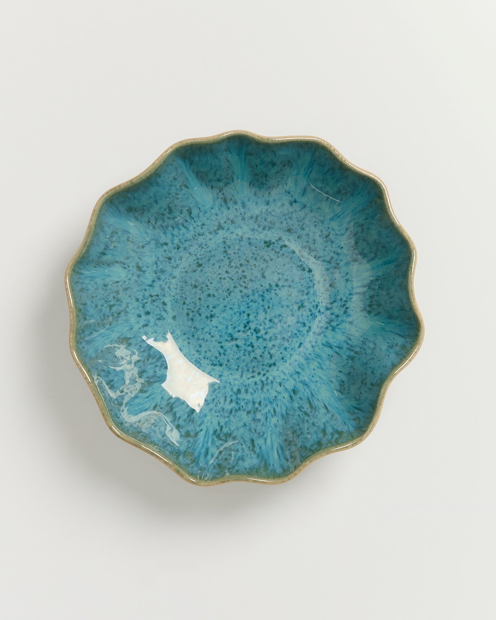 Eine blaugefärbte Keramikschale mit gewelltem Rand auf weißem Hintergrund.