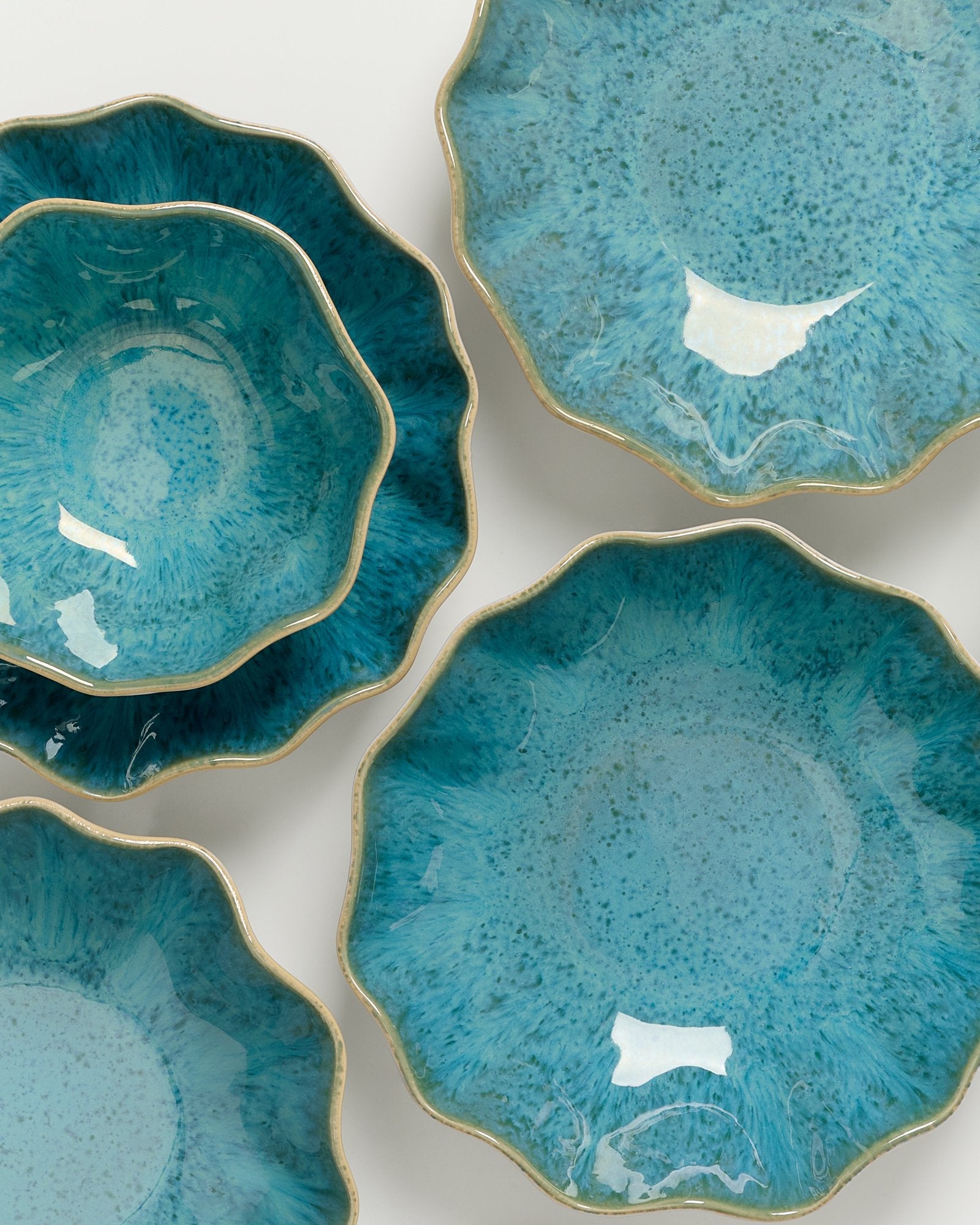 Türkisfarbene, blumenförmige Teller mit goldenen Rändern auf einer weißen Oberfläche.