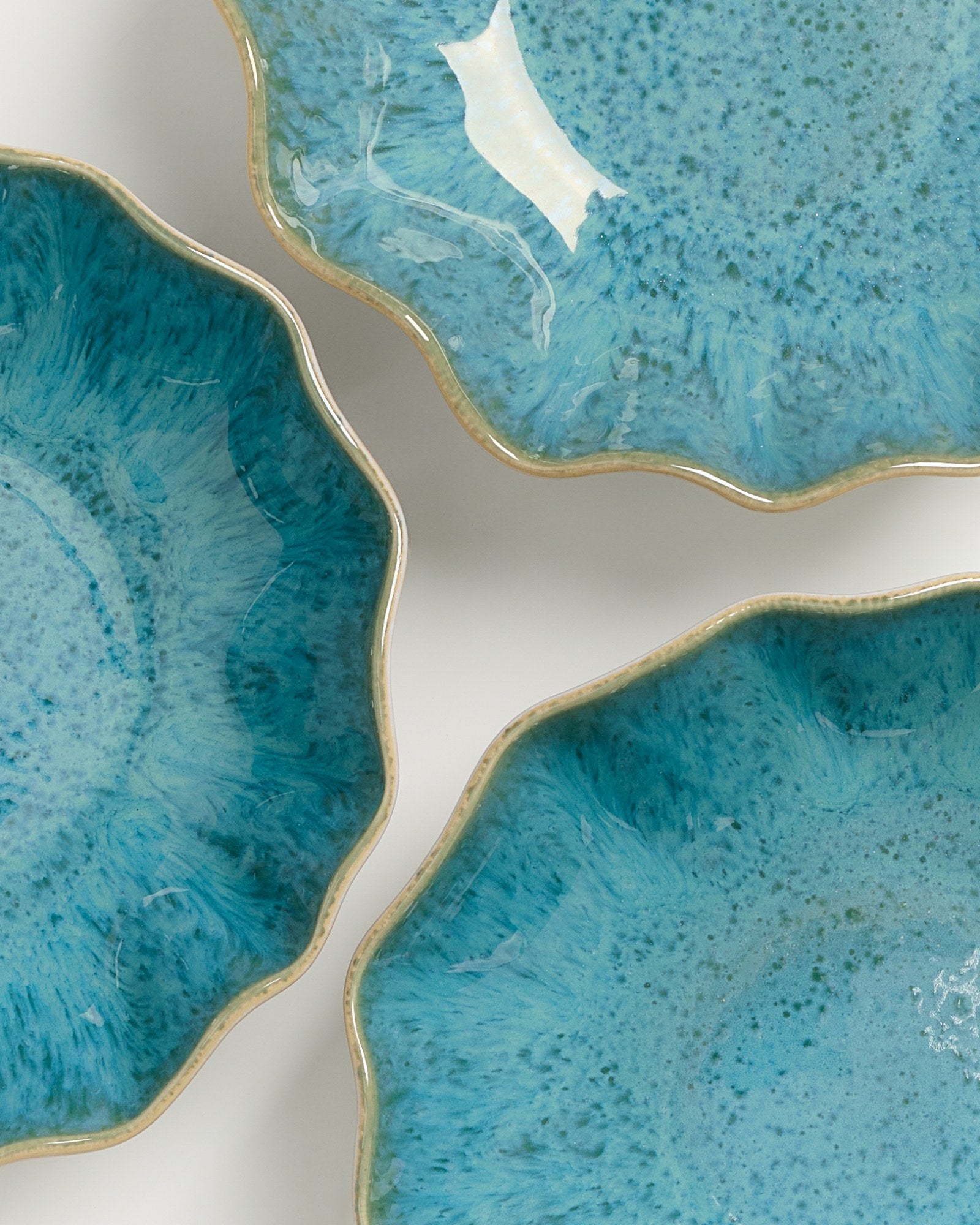 Drei blaue, muschelförmige Teller mit strukturierter Oberfläche und hellbraunem Rand auf weißem Hintergrund.