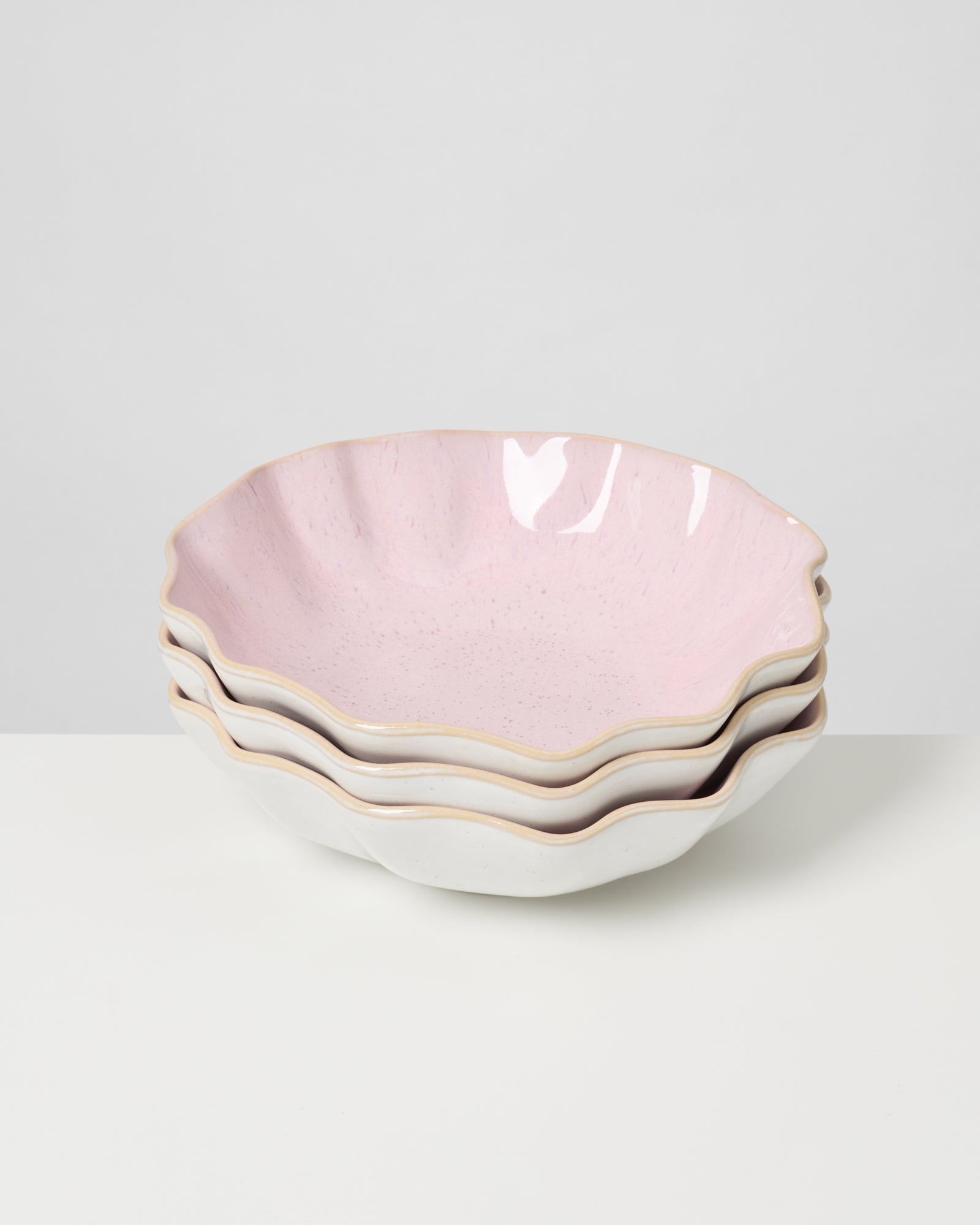 Vier übereinander gestapelte, pastellfarbene Schalen mit gewelltem Rand auf weißem Hintergrund.