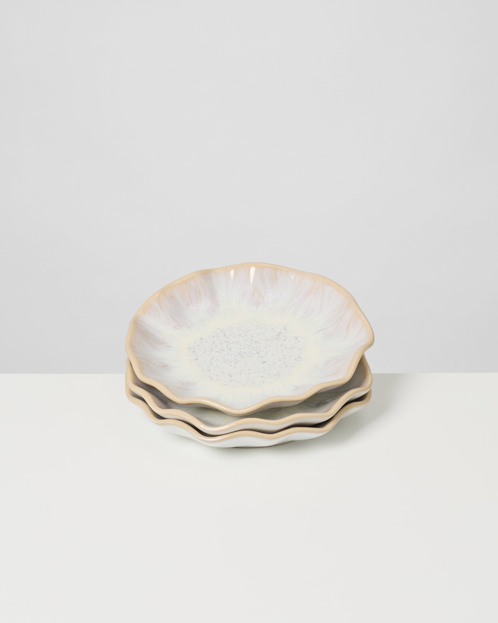 Drei dekorative, blütenförmige Teller in Pastelltönen auf einem weißen Tisch.