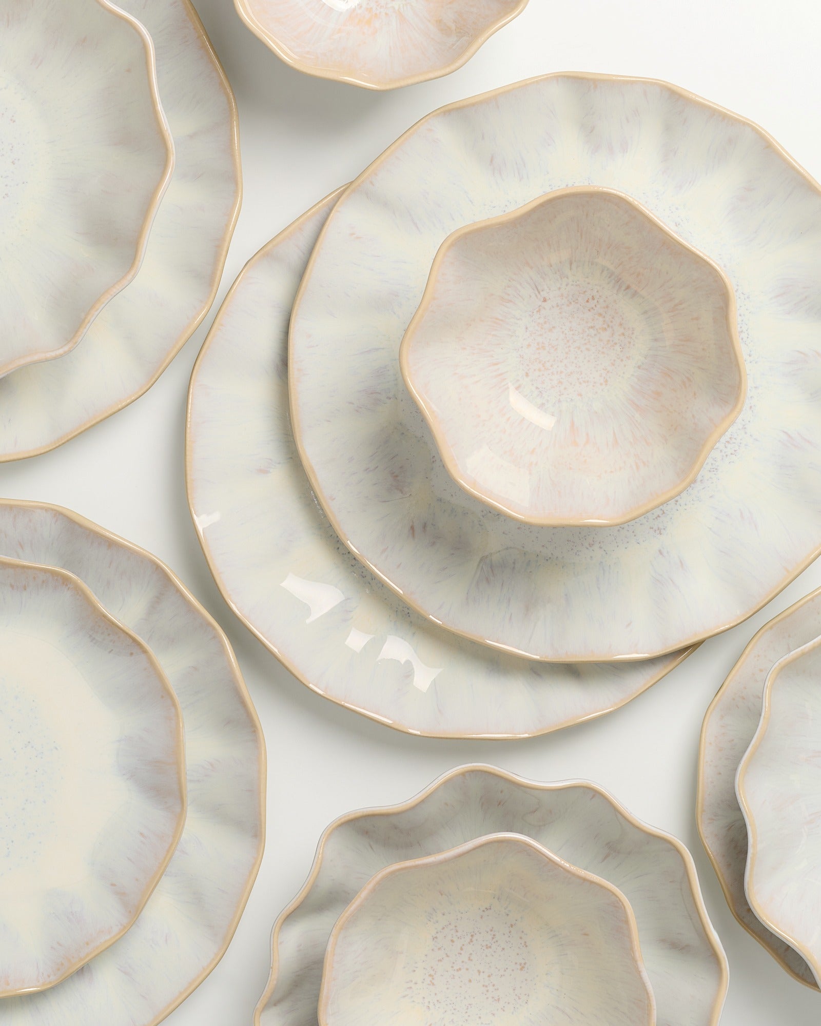 Mehrere keramikfarbene, gewellte Teller mit einem dezenten, marmorierten Design liegen übereinander auf weißem Hintergrund.