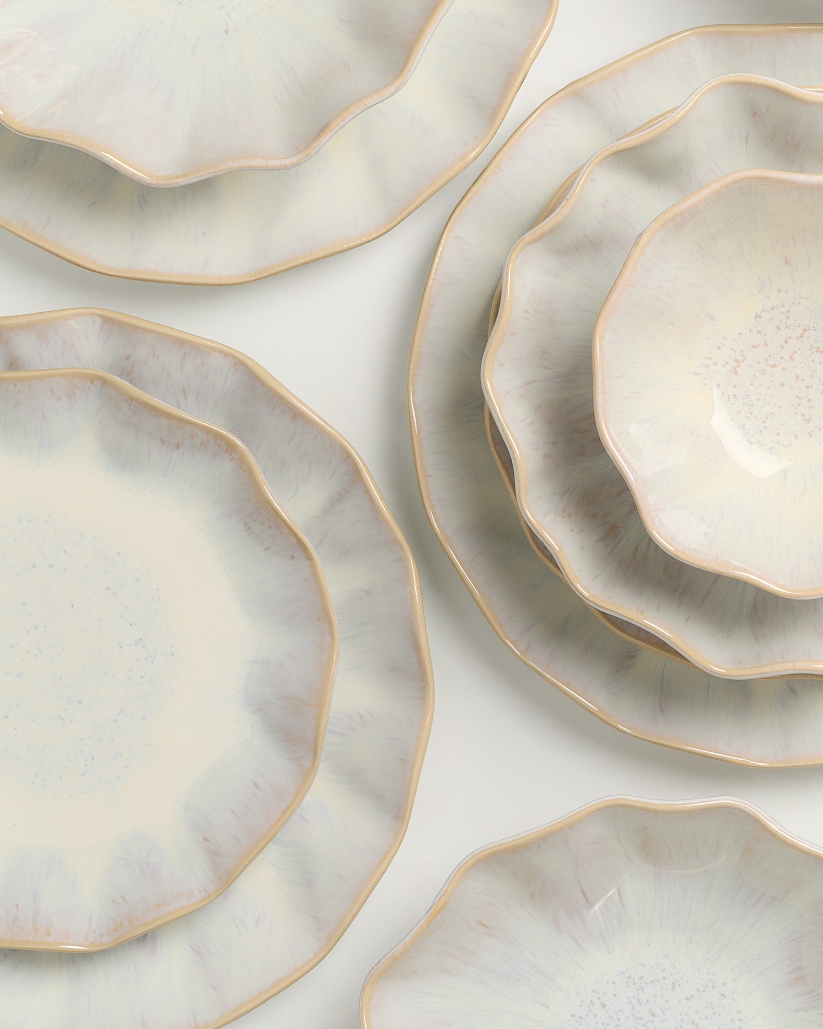Mehrere hellbeige Teller mit unregelmäßigen, gewellten Rändern liegen auf einer flachen Oberfläche.