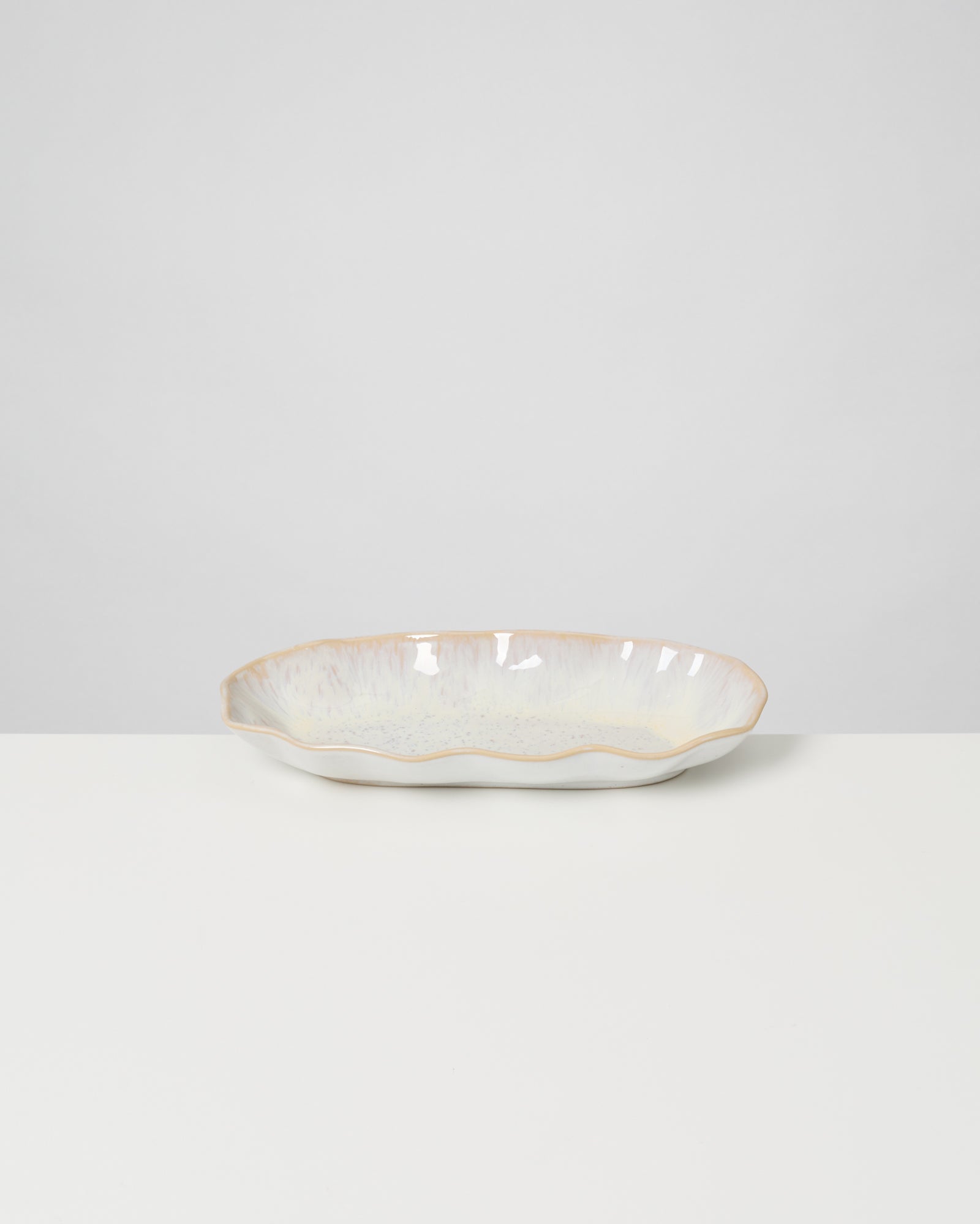 Ovale, weiß-glasierte Keramikschale mit gewelltem Rand auf weißem Hintergrund.