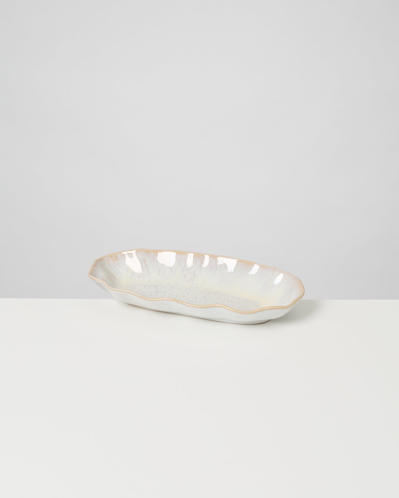 Keramikschale mit unregelmäßigem Rand in Pastellfarben steht auf einem weißen Tisch vor grauem Hintergrund.