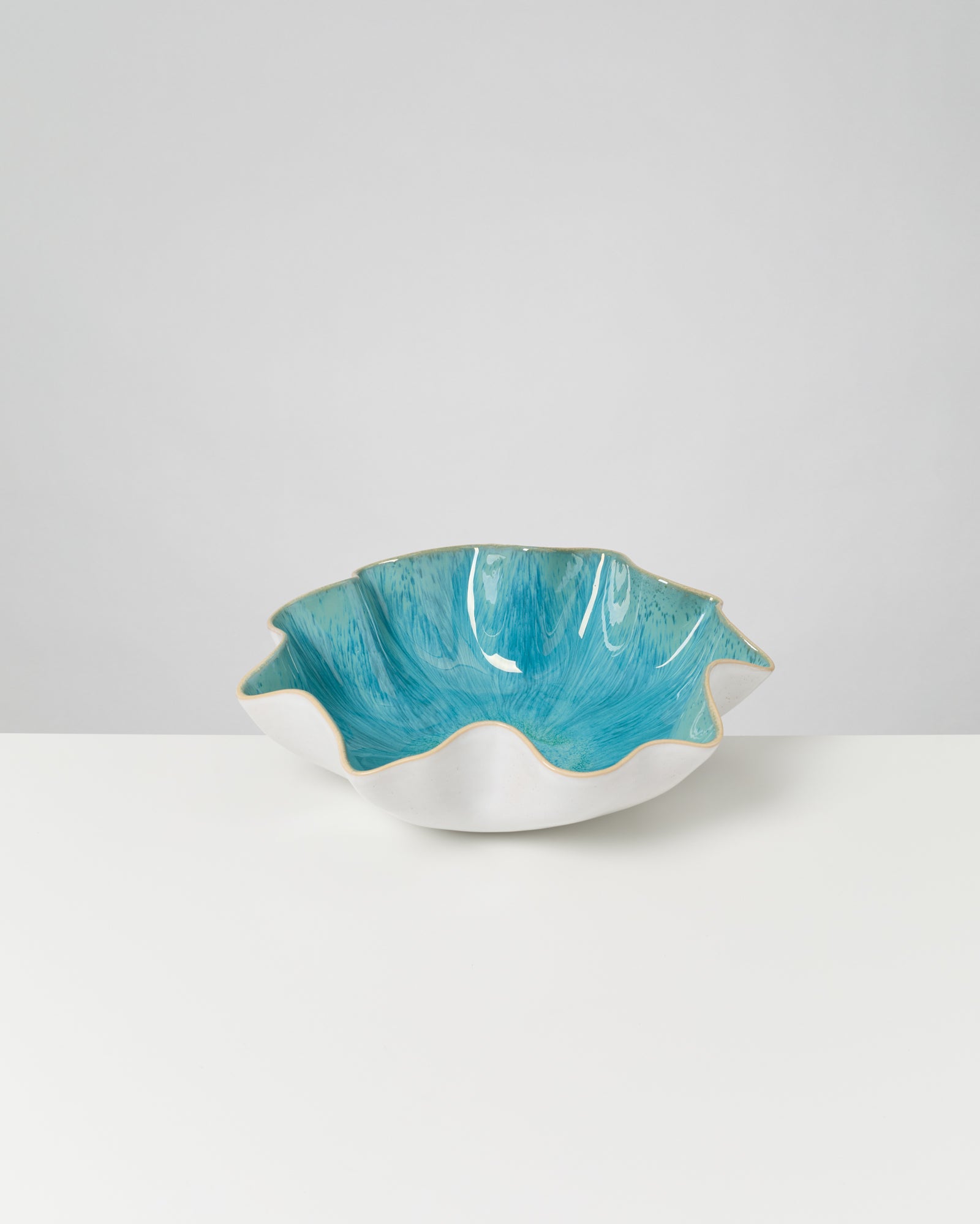 Dekorative weiße Schale mit wellenförmigem, türkisfarbenem Inneren auf weißem Tisch und grauem Hintergrund.