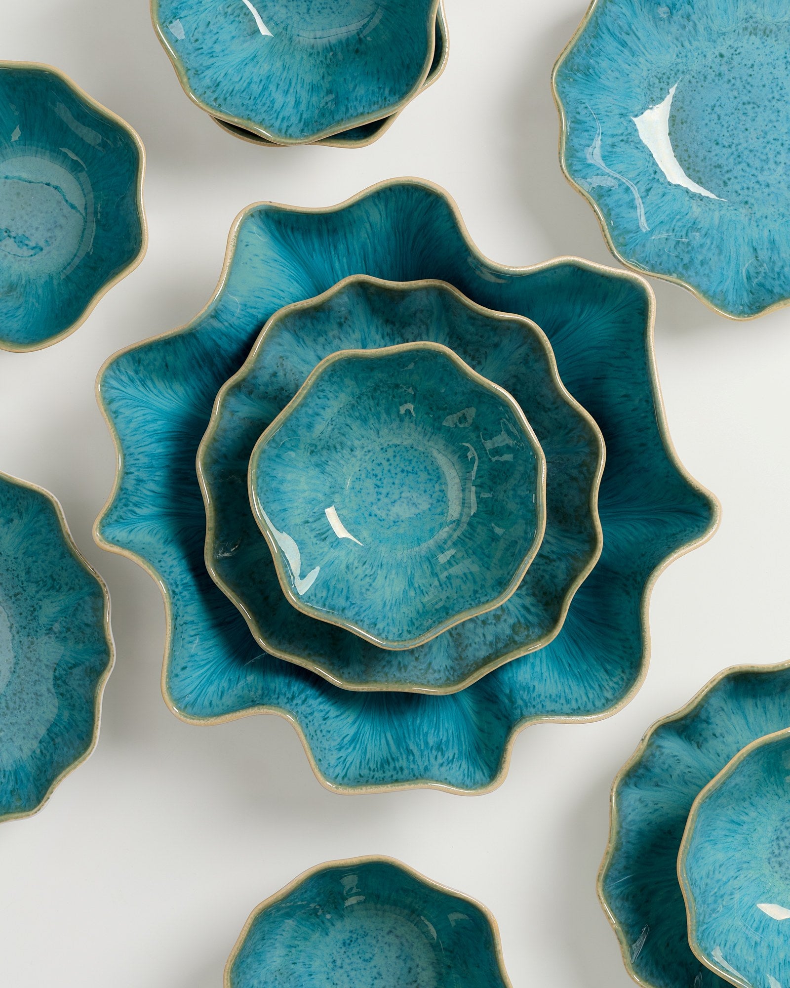 Verschiedene türkisfarbene, gewellte Keramikteller auf weißem Hintergrund angeordnet.