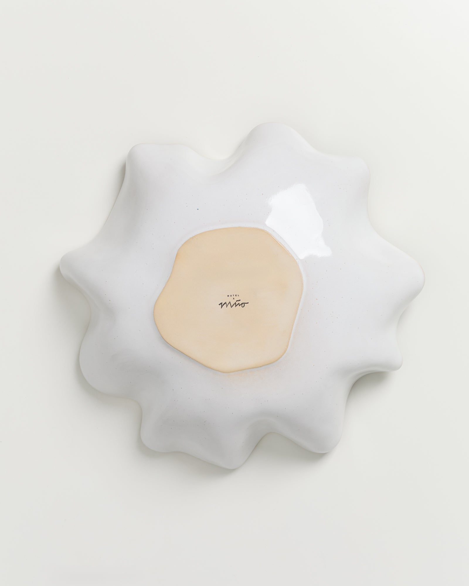 Weiße, wellenförmige Keramikskulptur mit einem beigefarbenen Zentrum auf weißem Hintergrund.