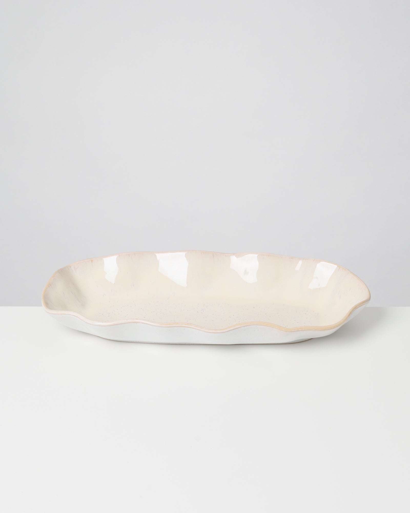 Ovale, cremefarbene Keramikschale mit welligem Rand auf einem weißen Untergrund.