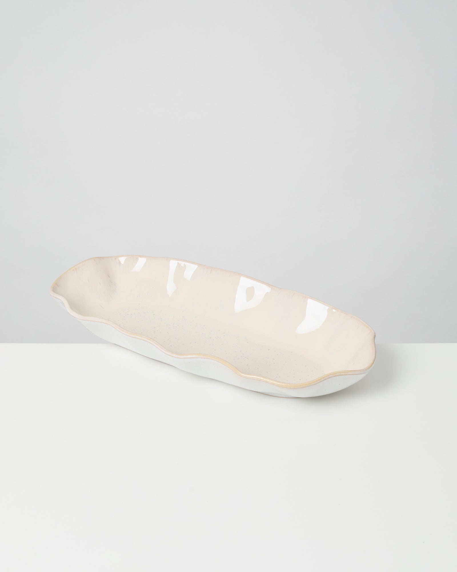 Längliche, cremefarbene Keramikschale mit gewelltem Rand, auf einem weißen Untergrund.