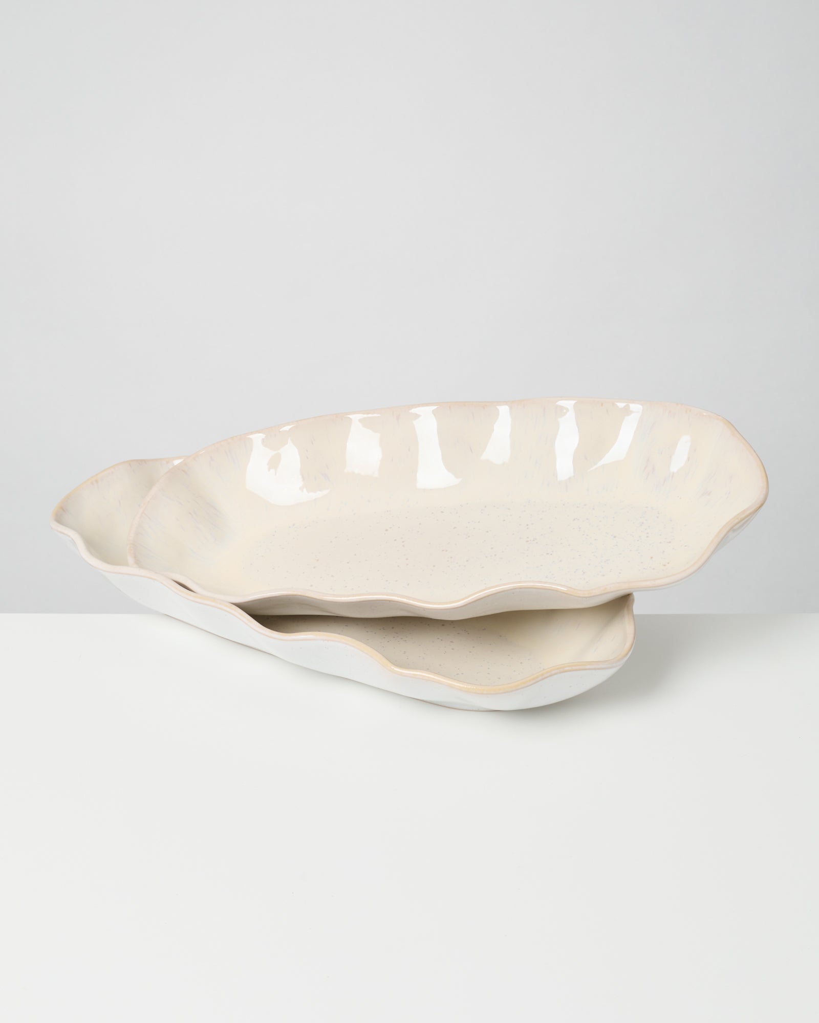 Zwei übereinander gestapelte, ovale Keramikschalen mit welligem Rand auf weißem Hintergrund.