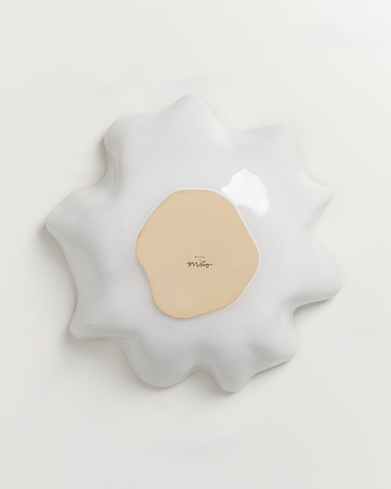 Abstrakte, wellenförmige Skulptur in Weiß mit beiger Mitte und handschriftlichem Text auf hellem Hintergrund.