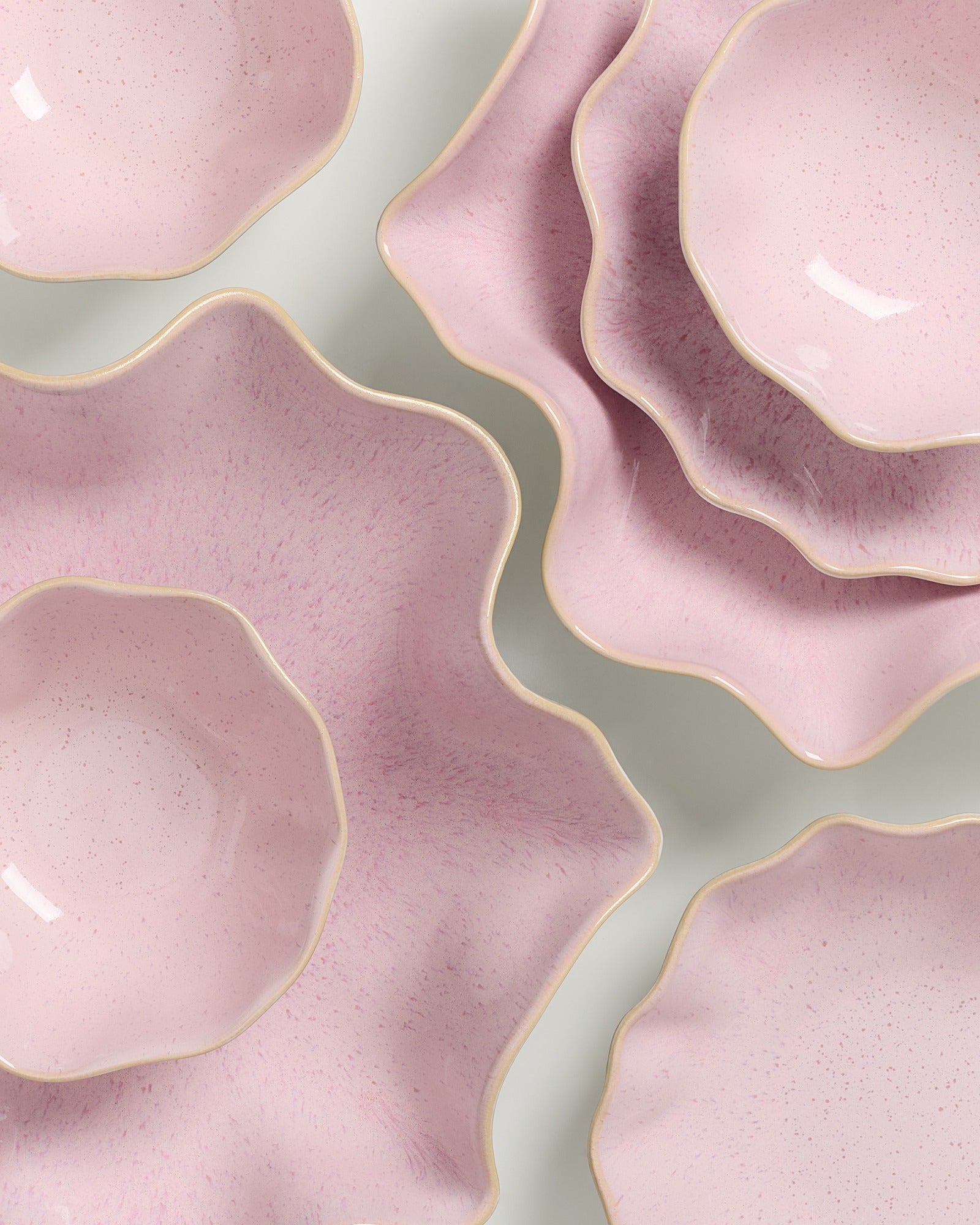 Rosa, blütenförmige Teller mit gewellten Rändern auf grauem Hintergrund.