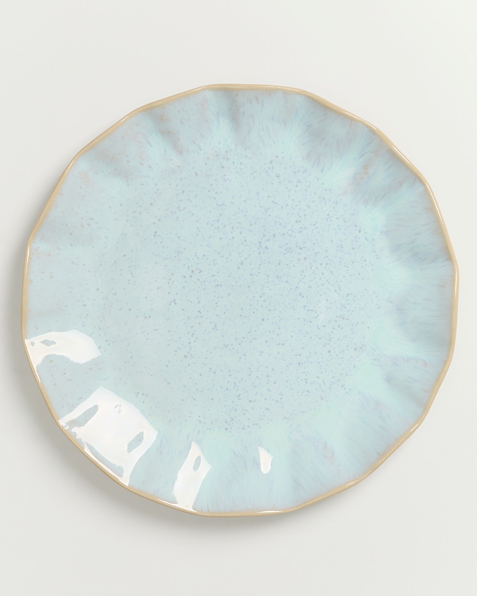 Helltürkiser, keramikartiger Teller mit unregelmäßigem Rand und beigem Rand auf weißem Hintergrund.