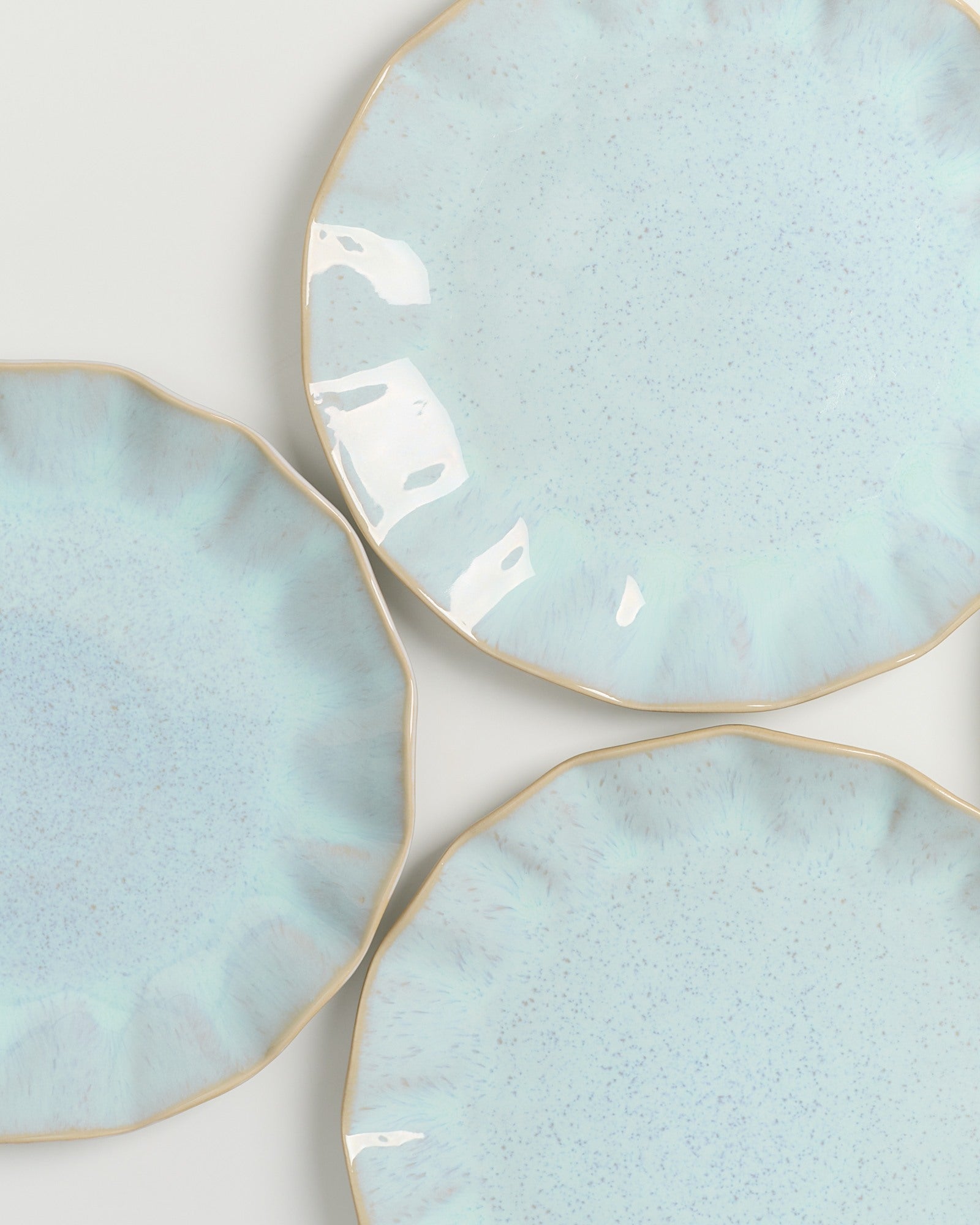 Drei hellblaue Teller mit unregelmäßigen Rändern und goldener Umrandung auf einer weißen Oberfläche.