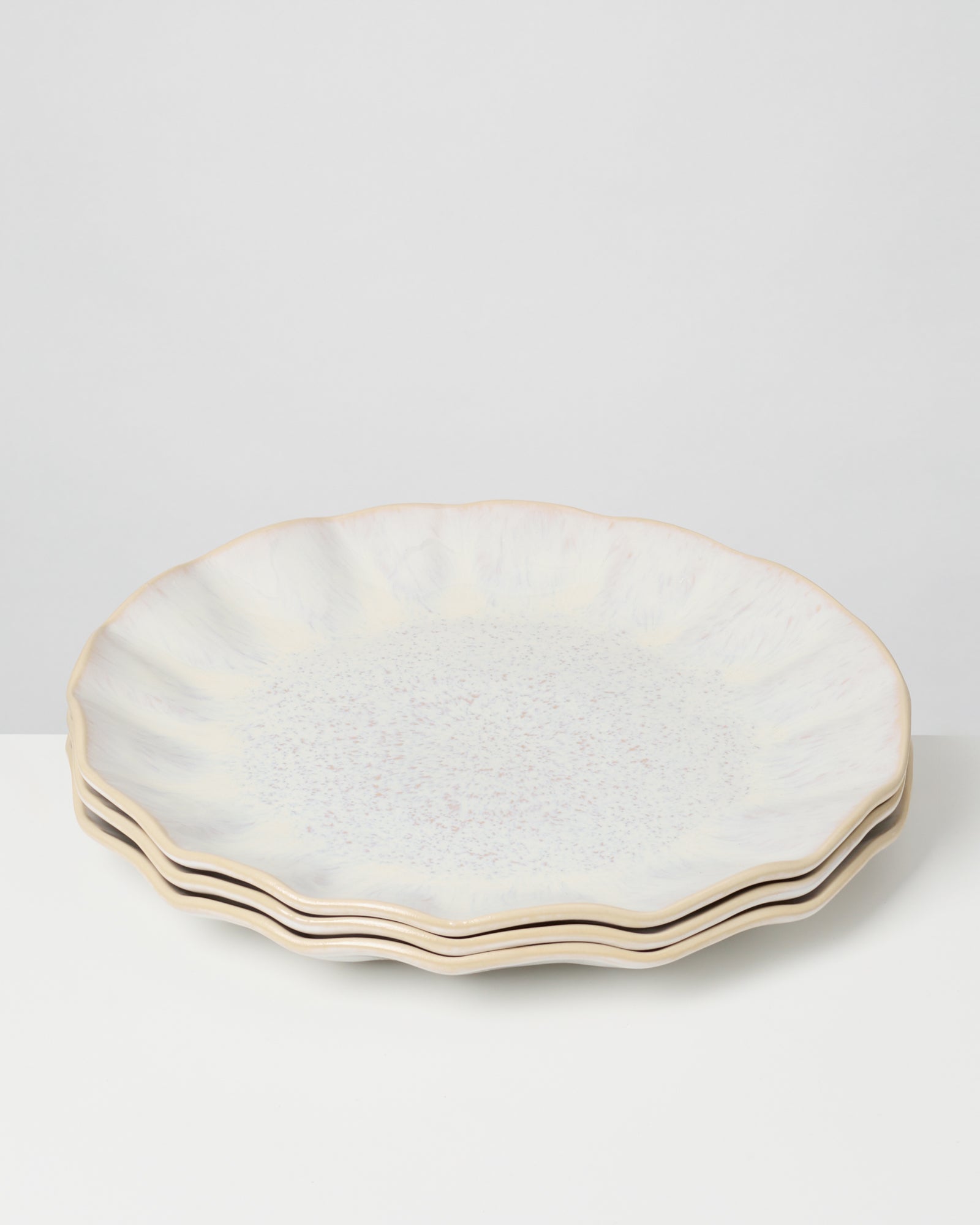 Drei gestapelte Teller mit welligem Rand und blassmarmoriertem Muster auf einem weißen Hintergrund.