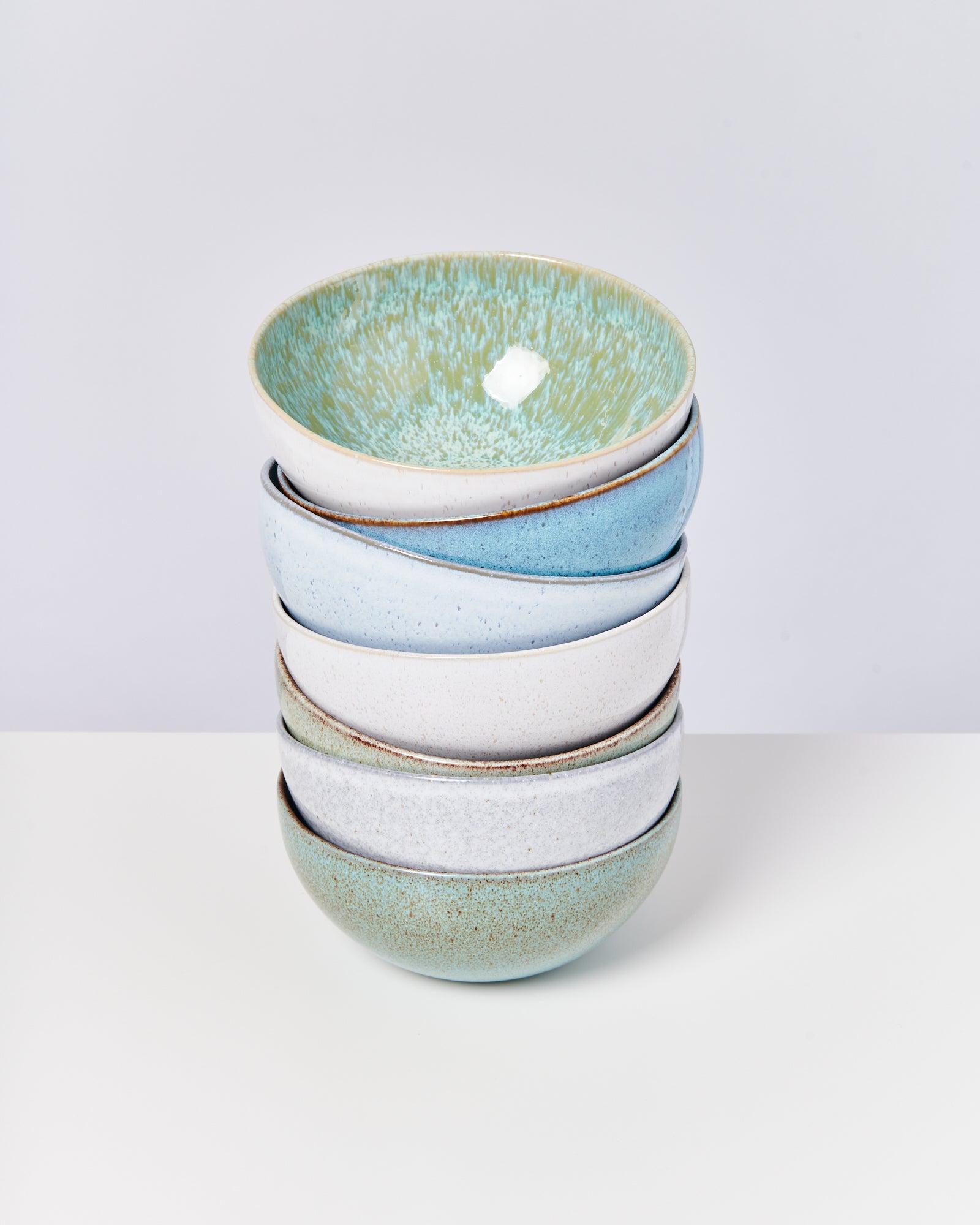 Ein Stapel von fünf keramikfarbenen Schalen in verschiedenen Pastelltönen steht auf einer weißen Oberfläche.