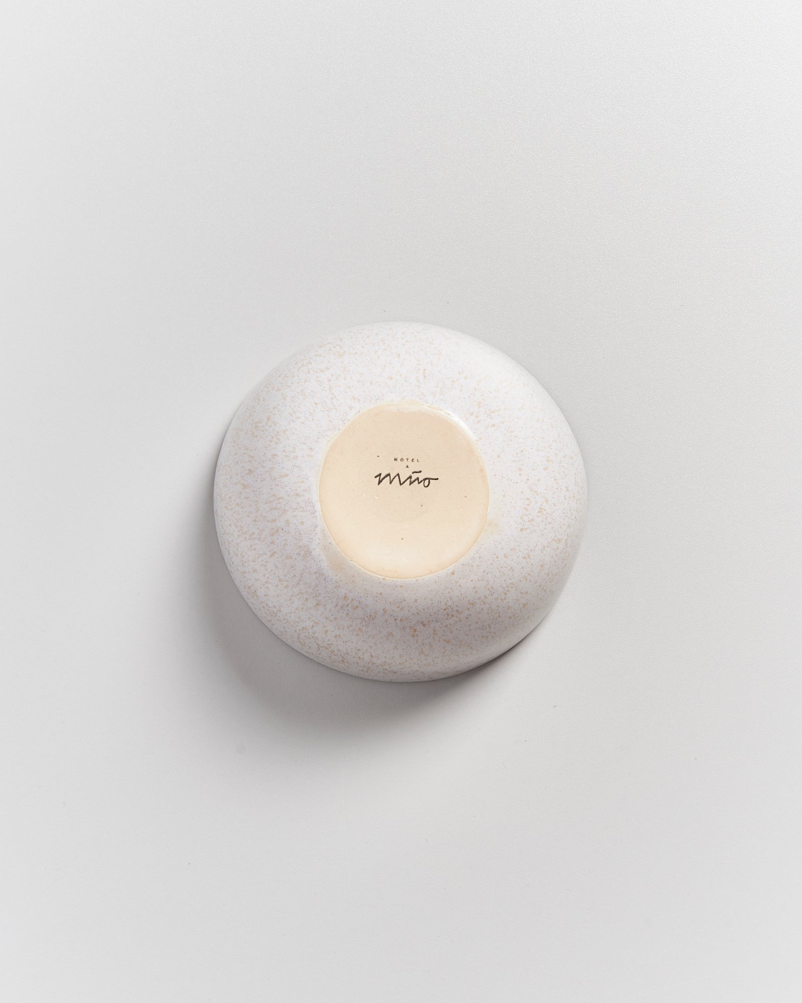 Runder, cremefarbener Keramikgegenstand auf einer hellen Oberfläche, mit der Aufschrift "Hotel Miró" auf der Unterseite.