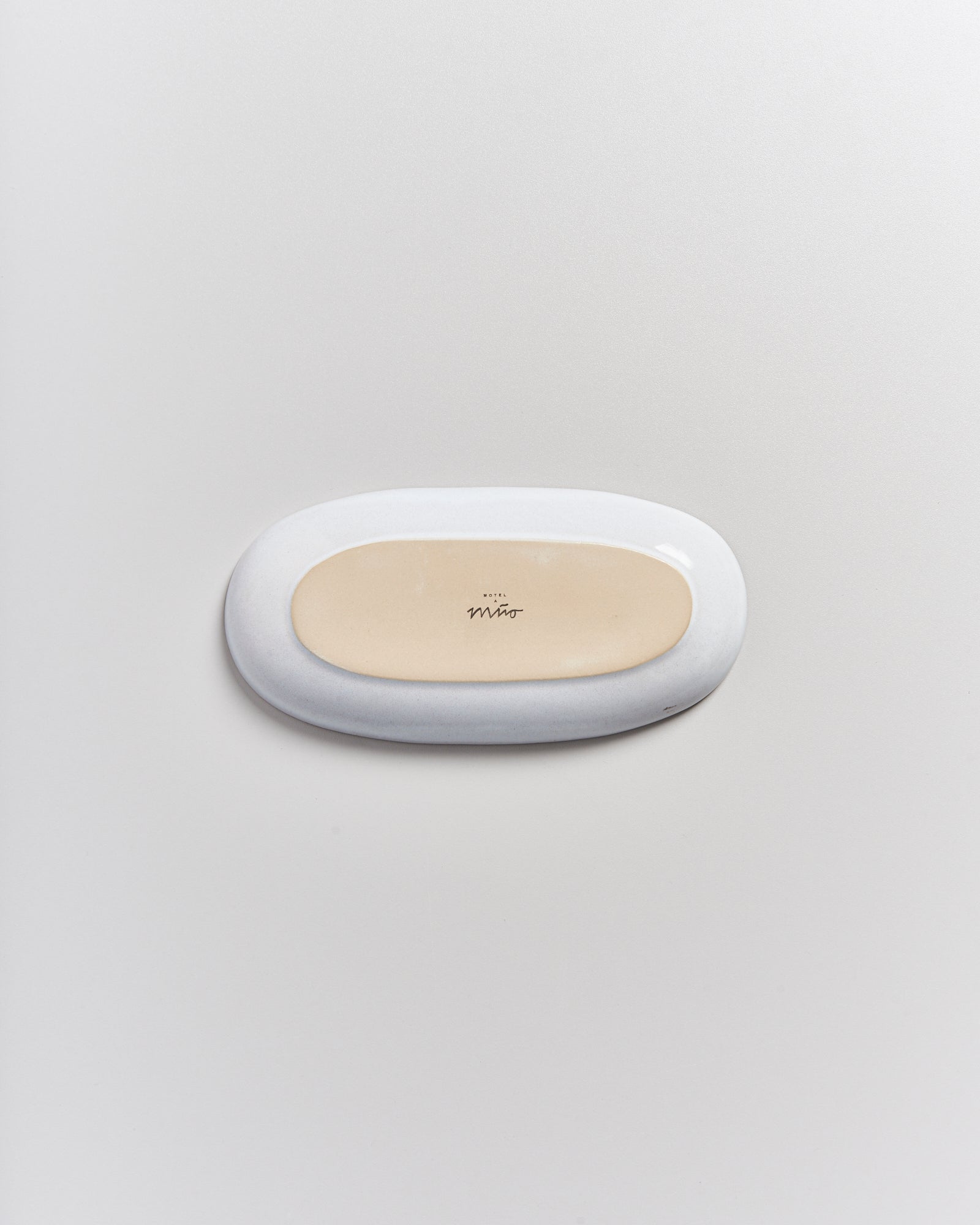 Ovale Seifenschale auf grauem Hintergrund, mit cremefarbener Mitte und dem Schriftzug "mio".