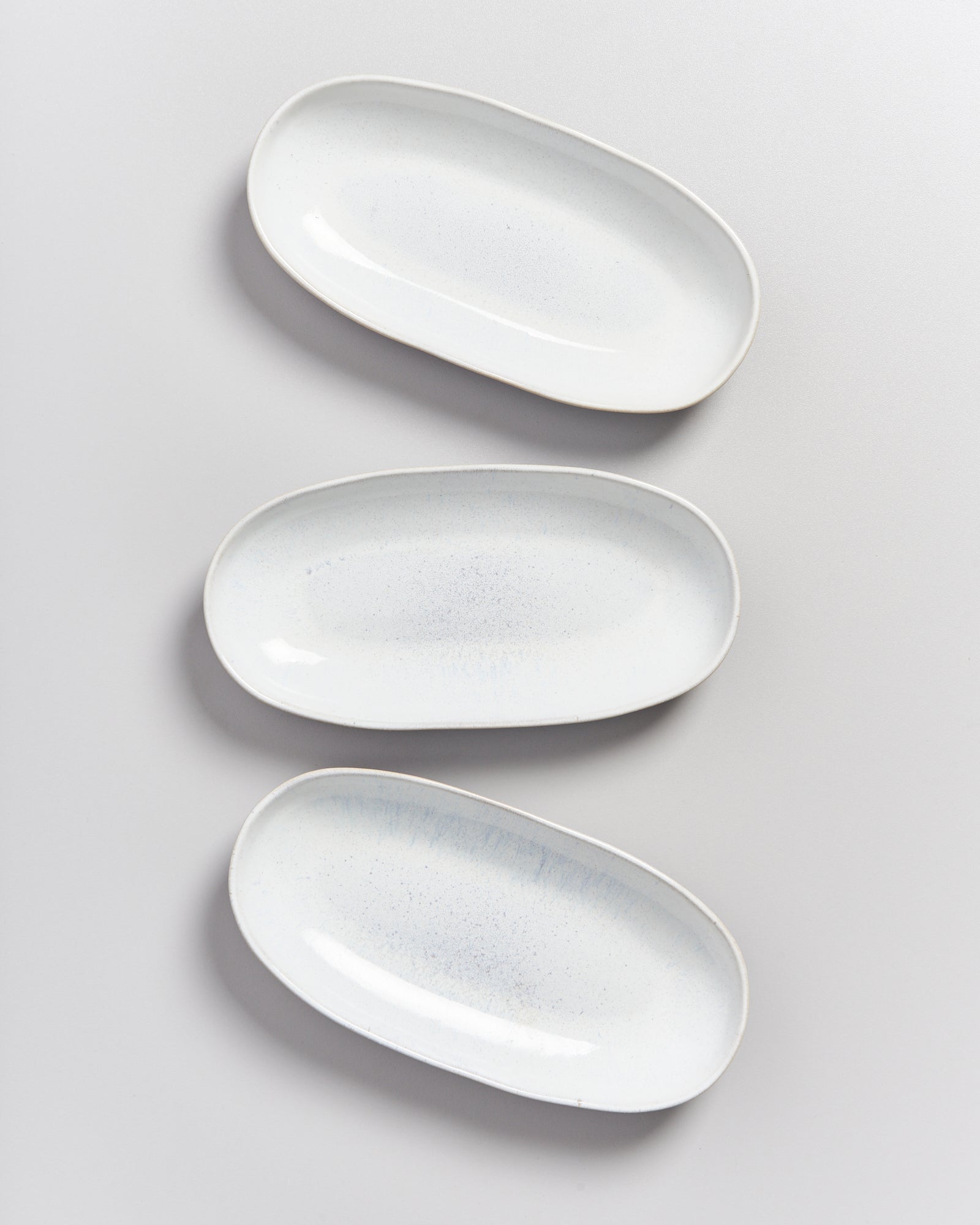 Drei weiße ovale Teller sind ordentlich nebeneinander auf einer hellen Oberfläche angeordnet.