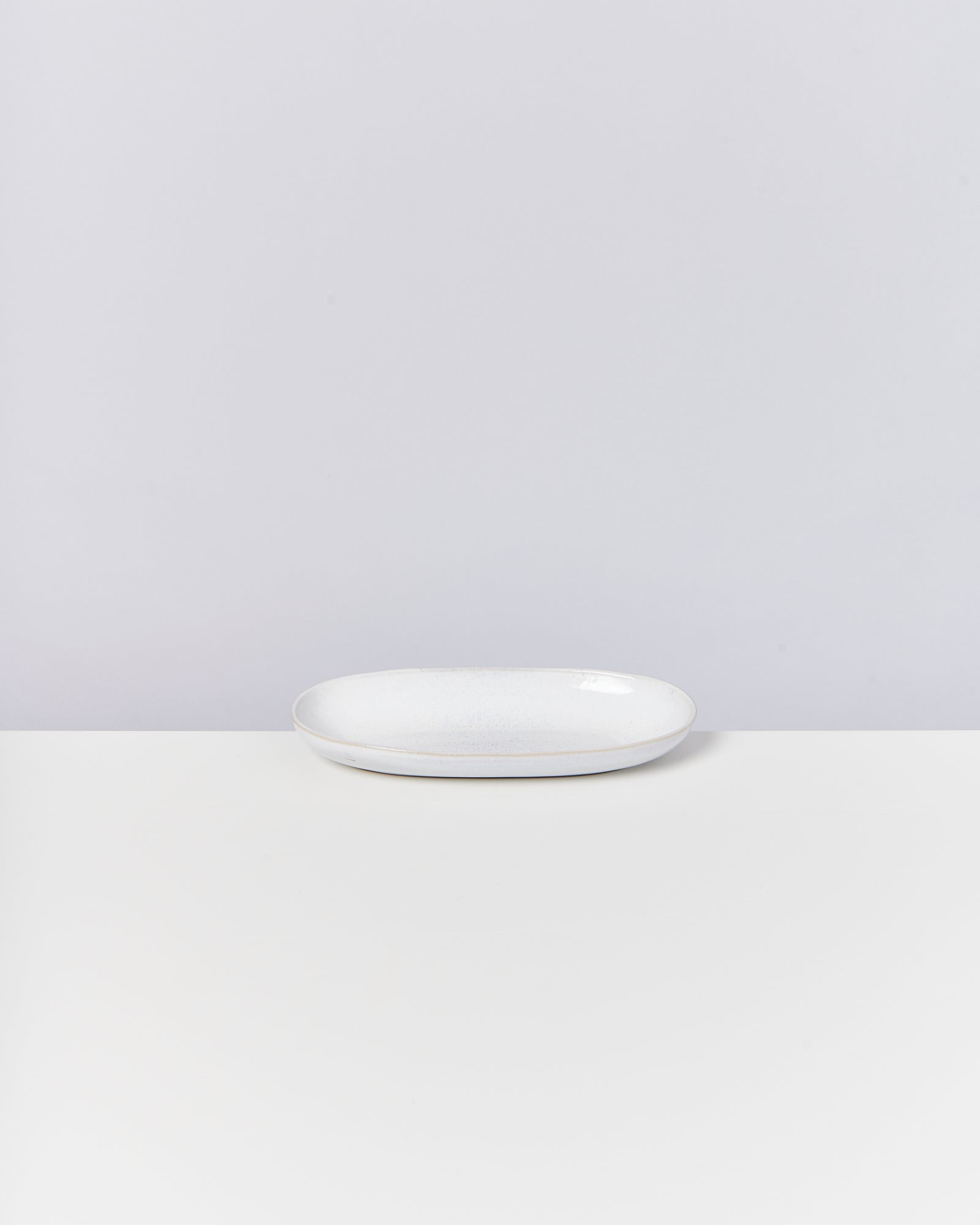 Weiße ovale Platte auf einem weißen Tisch vor einem hellgrauen Hintergrund.