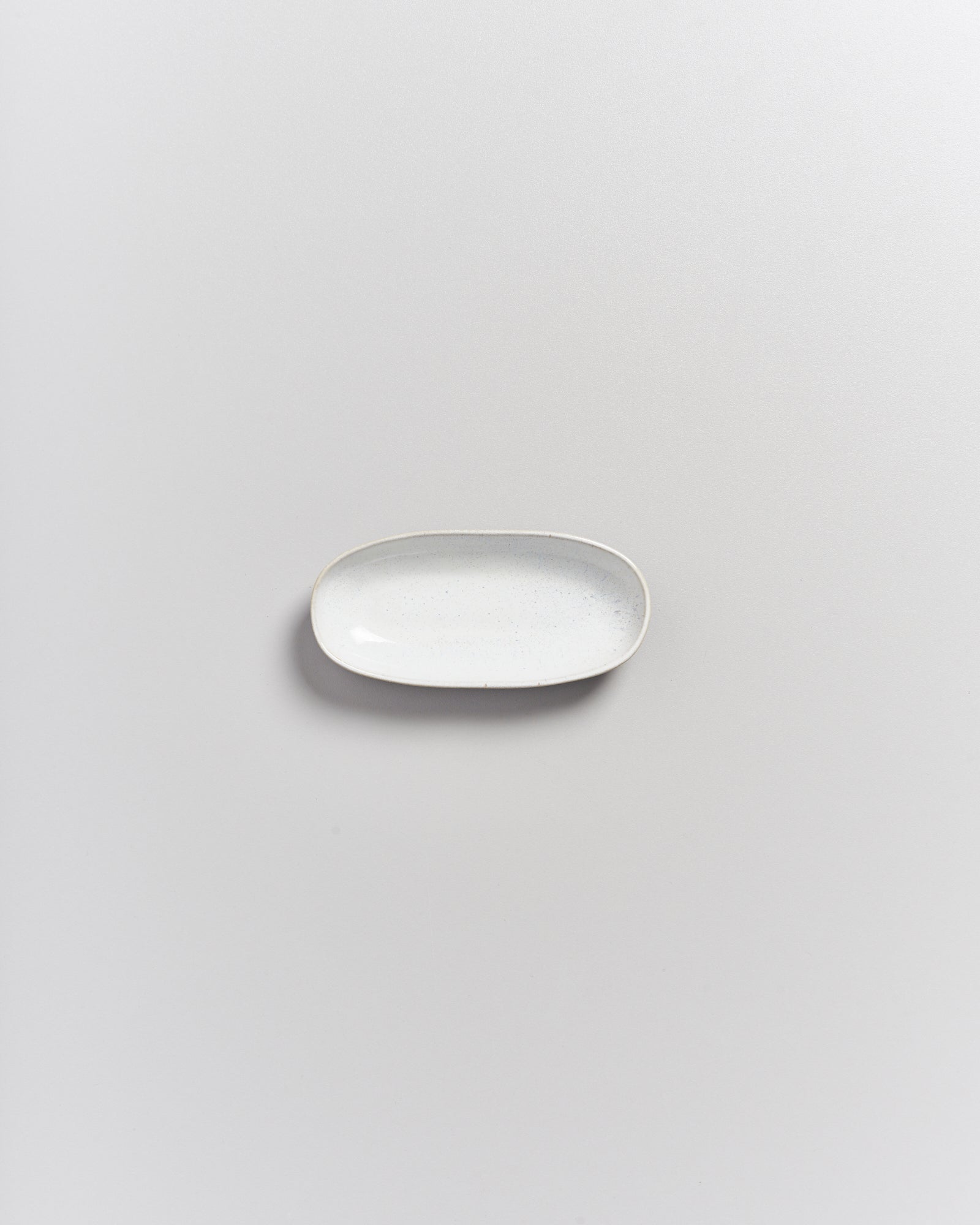 Kleine, ovale, weiße Keramikschale auf einer grauen Oberfläche.