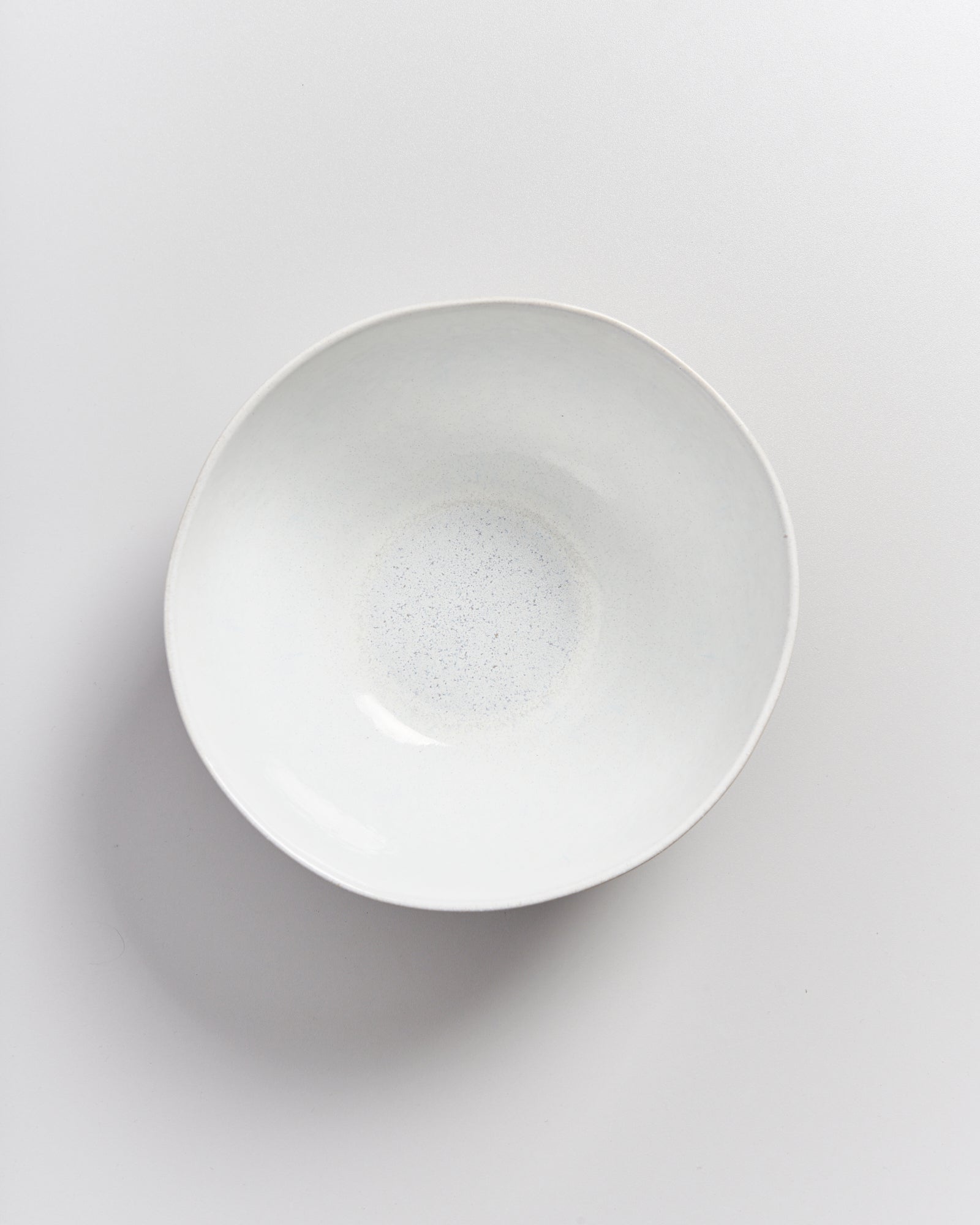Weiße, runde Keramikschale auf einem hellen Hintergrund, von oben fotografiert.