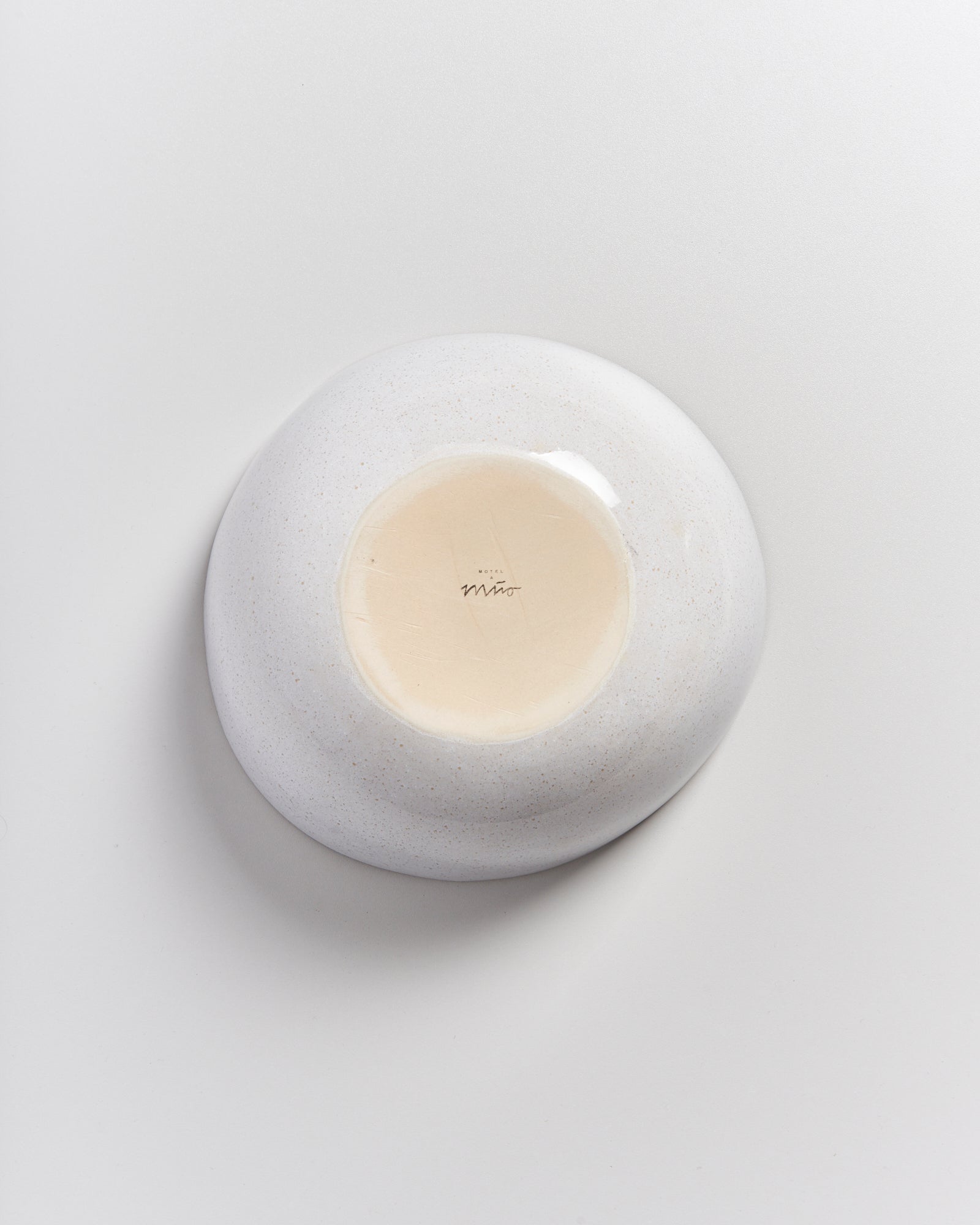 Rückseite einer weißen Keramikschale mit einer glatten, glasigen Basis, auf der ein Schriftzug zu sehen ist.