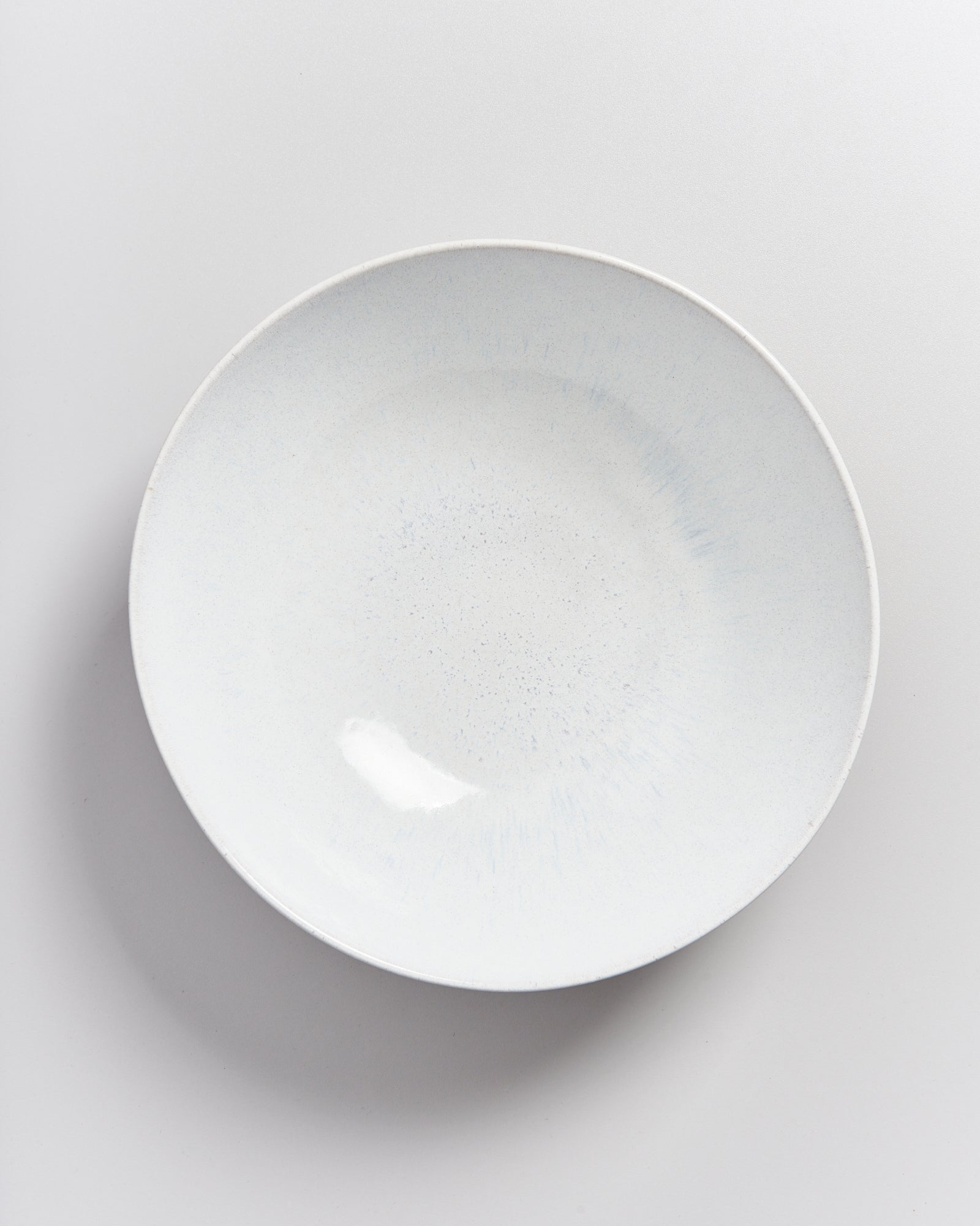 Ein weißer, leerer Teller mit dezentem Muster auf einer hellen Oberfläche.