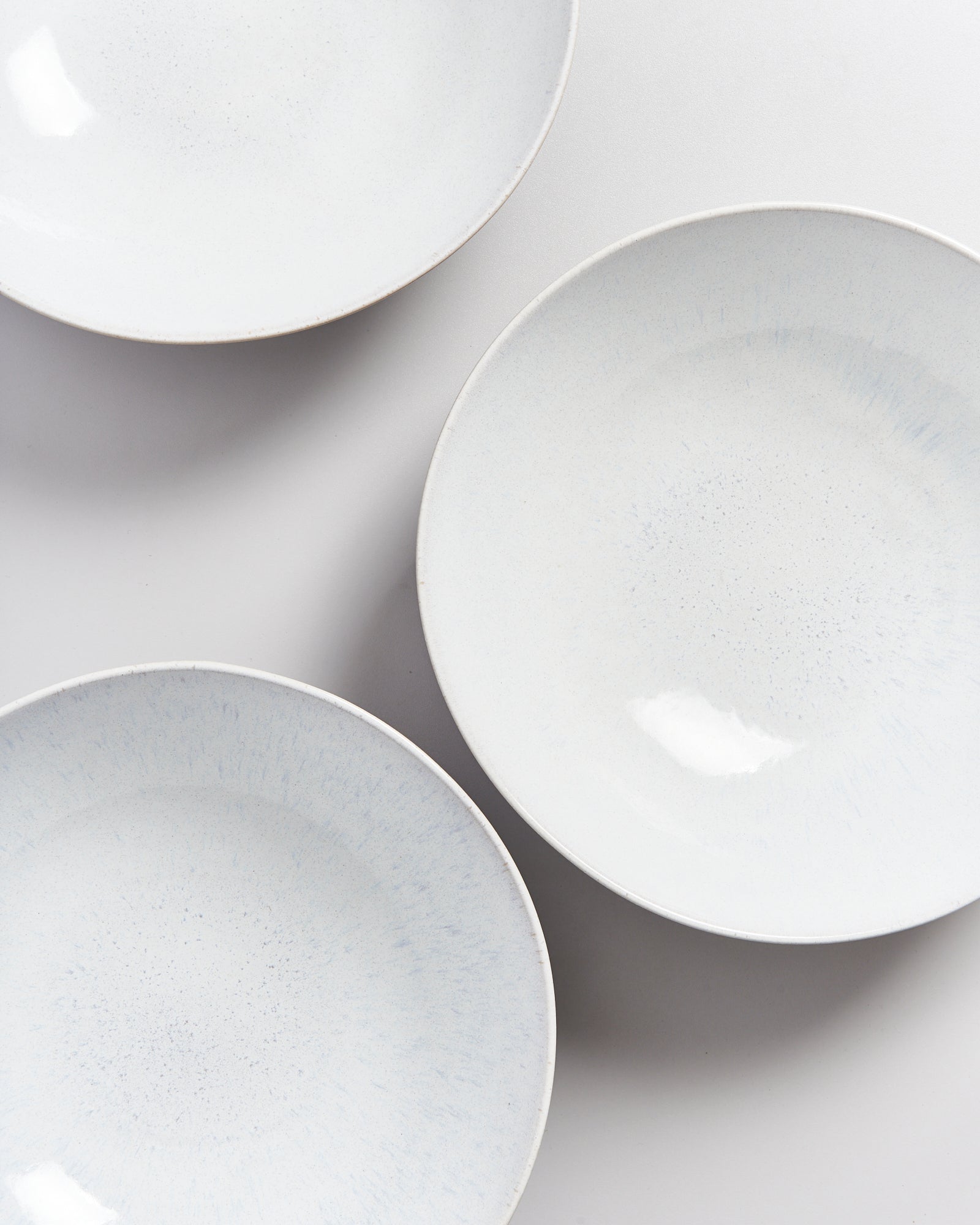 Drei weiße, runde Teller mit leichtem Muster auf einem weißen Hintergrund.