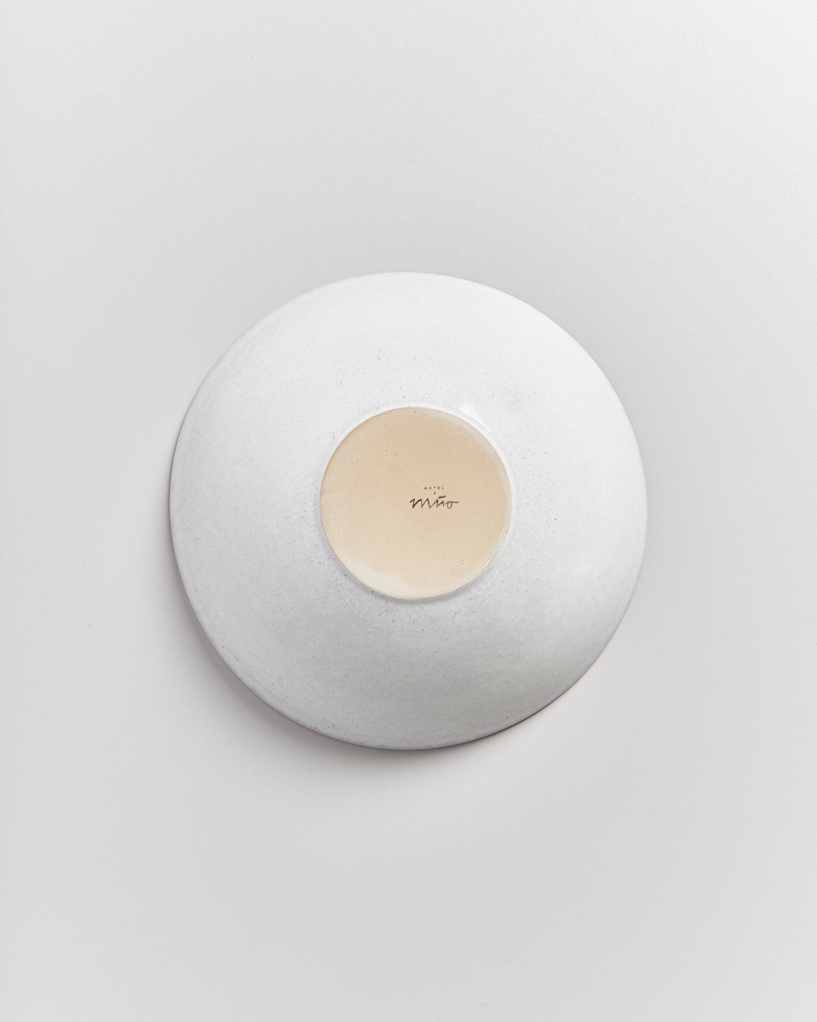 Weiße Keramikschale mit einem beige zentrierten Bereich auf der Unterseite, auf einer hellgrauen Oberfläche liegend.