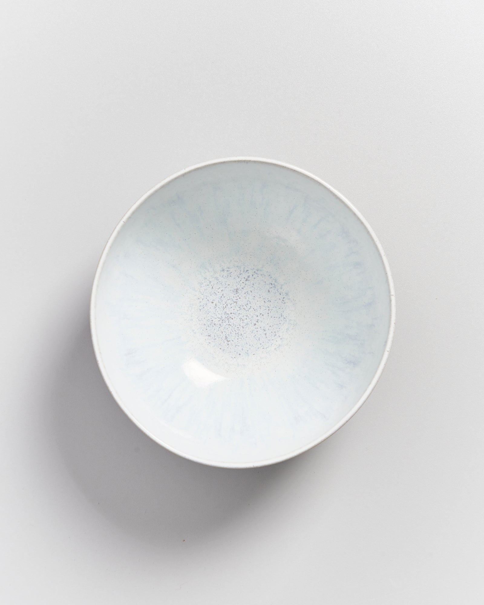 Eine flache, helle Keramikschale mit dezentem Muster steht auf einem weißen Hintergrund.