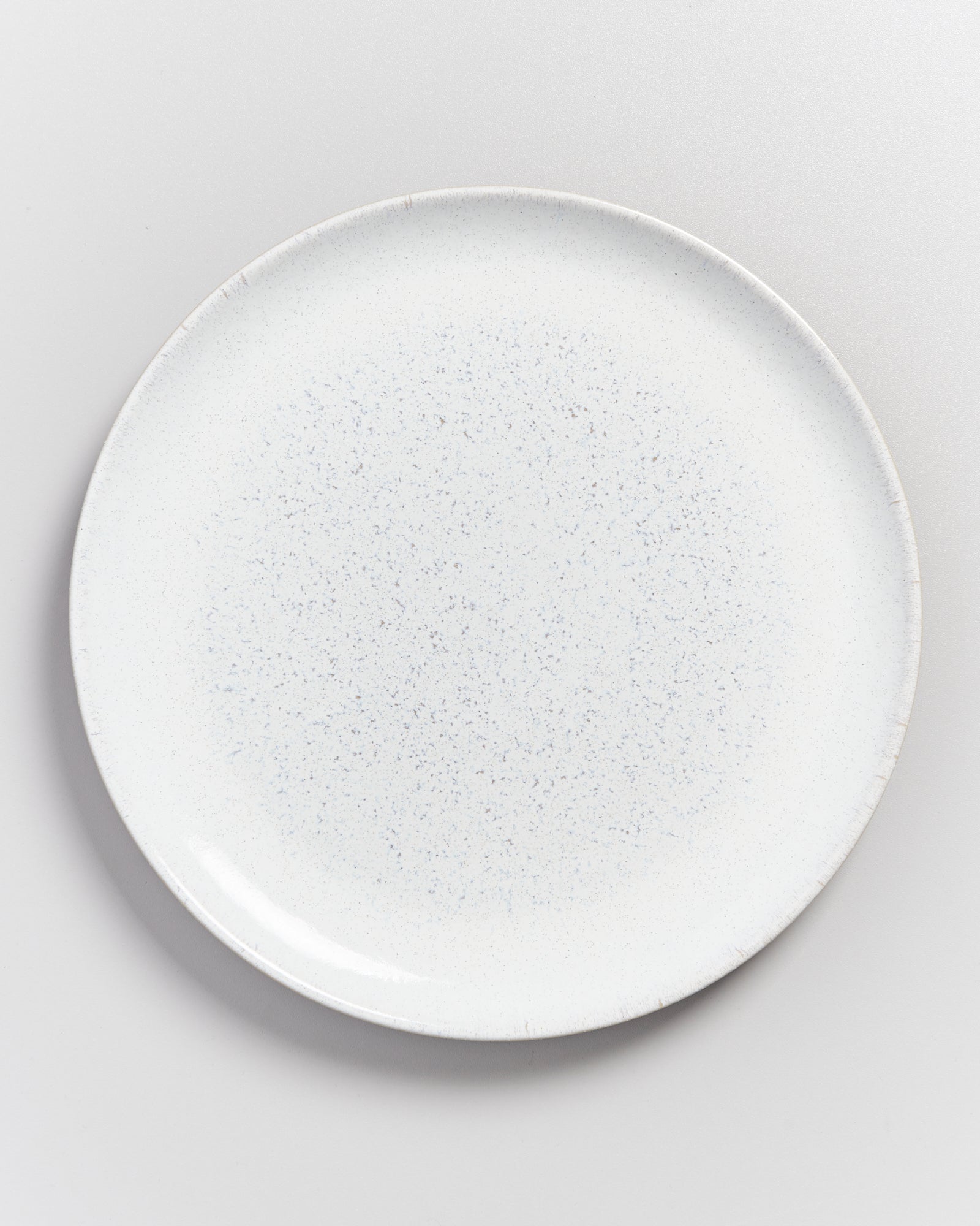 Ein runder, weißer Teller mit feinen blauen Sprenkeln steht auf einer grauen Oberfläche.