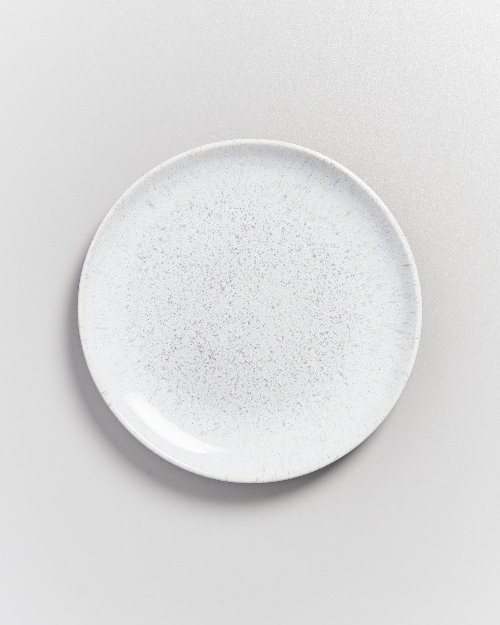 Weiße, runde Keramikplatte mit einem leicht gesprenkelten Muster auf einer hellgrauen Oberfläche.