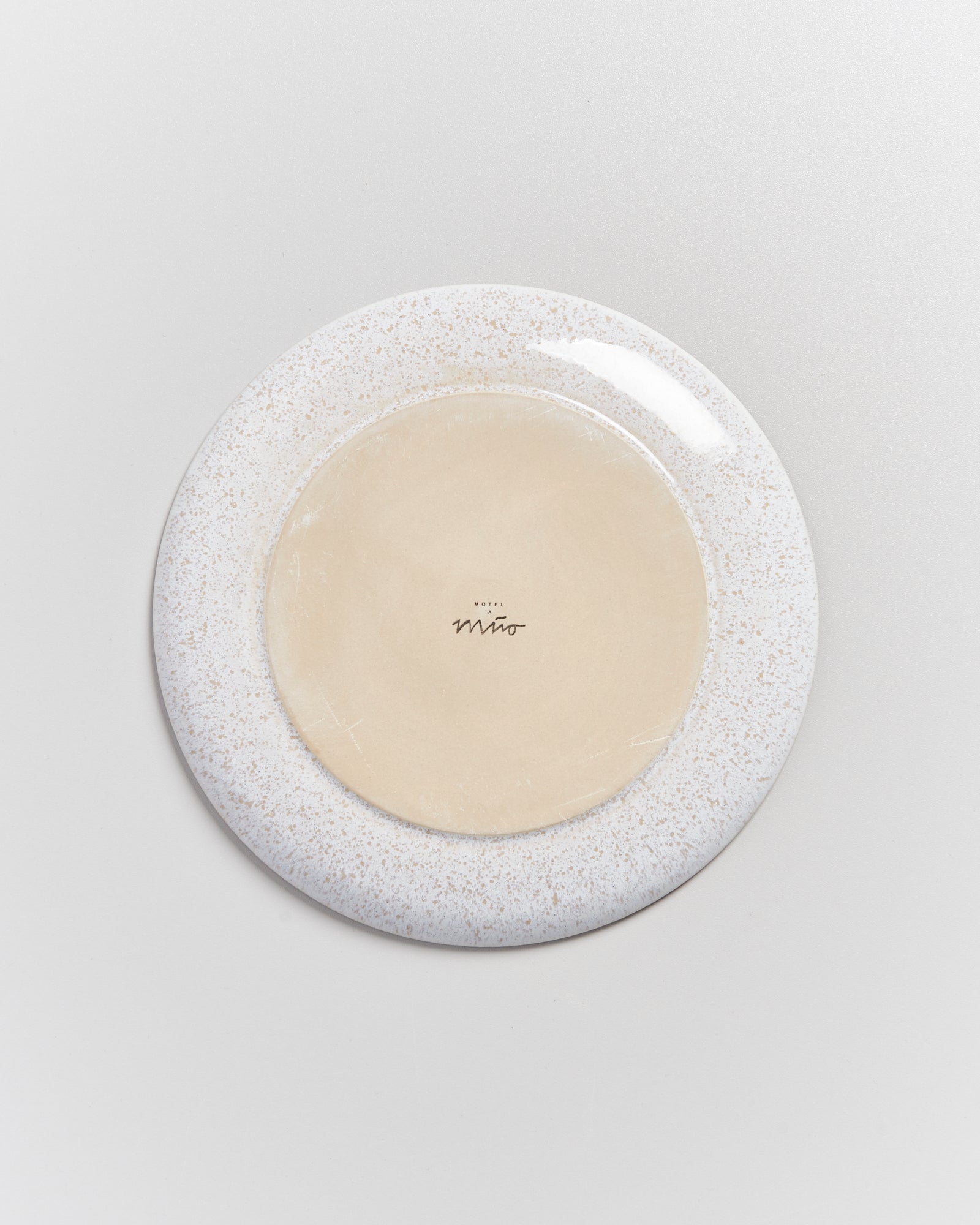 Runde Keramikplatte mit weißem Rand und beiger Mitte, auf der "Hotel Miró" steht, auf grauem Hintergrund.