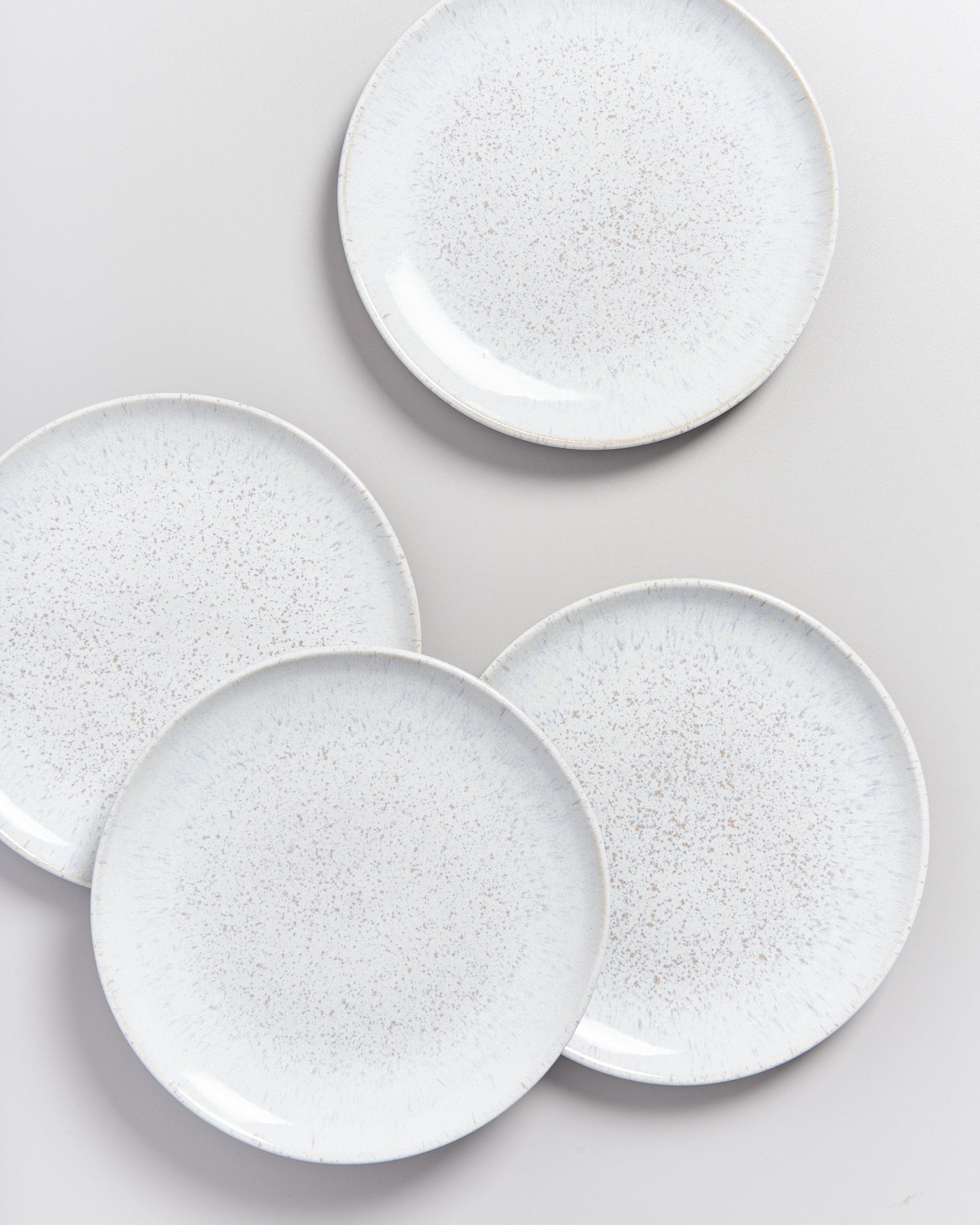 Vier weiße, gesprenkelte Teller auf einem grauen Hintergrund.