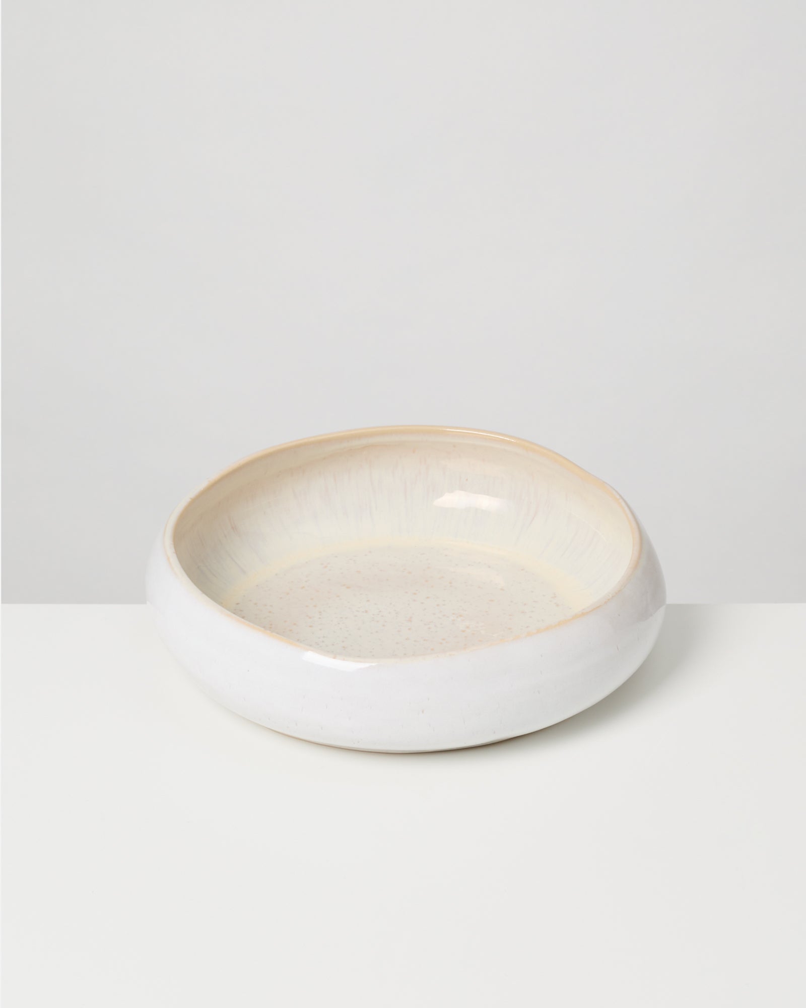 Weiße, runde Keramikschale mit breitem Rand auf weißem Hintergrund.