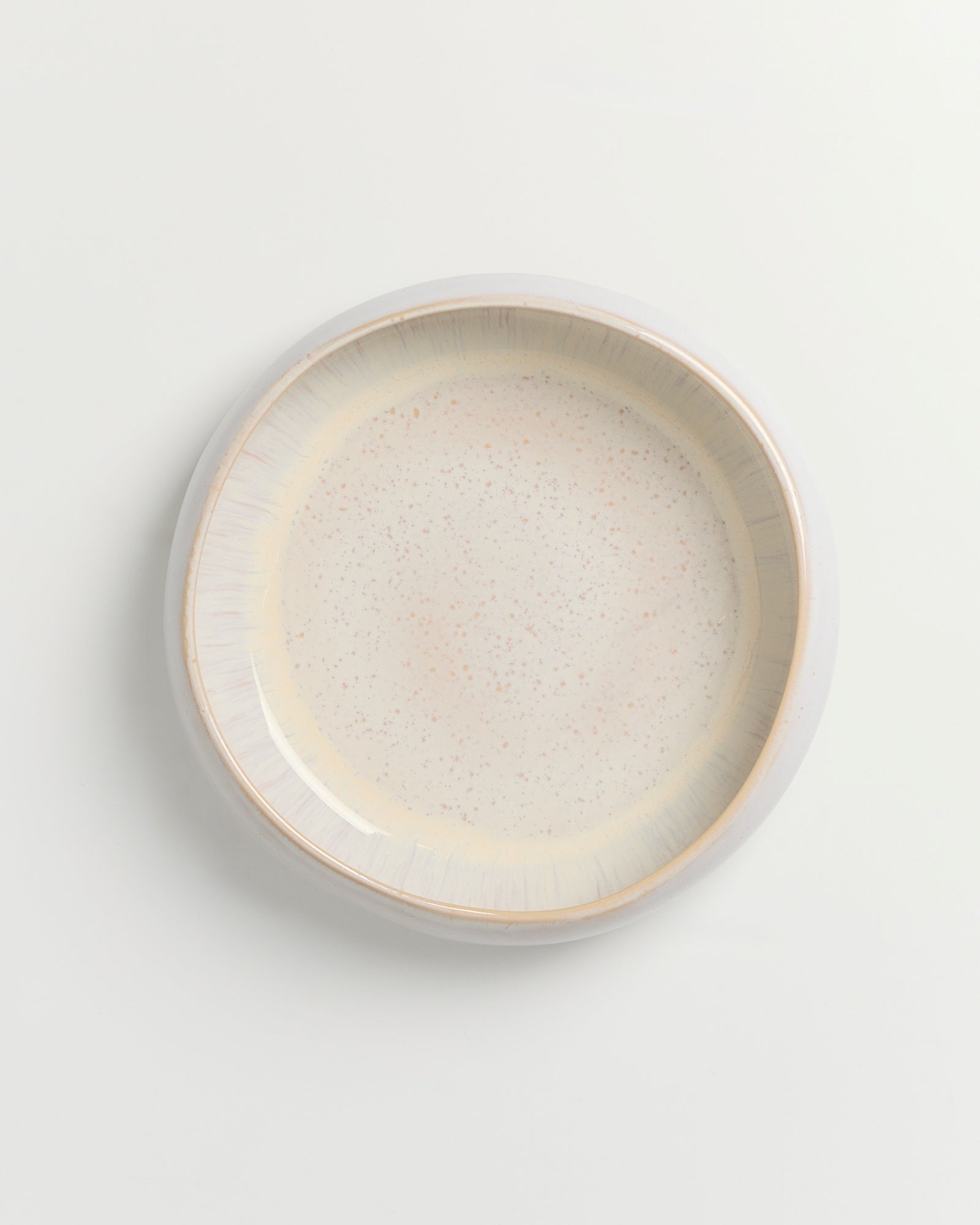 Keramikteller mit hellen, beigen und gesprenkelten Glasurdetails auf weißem Hintergrund, von oben betrachtet.