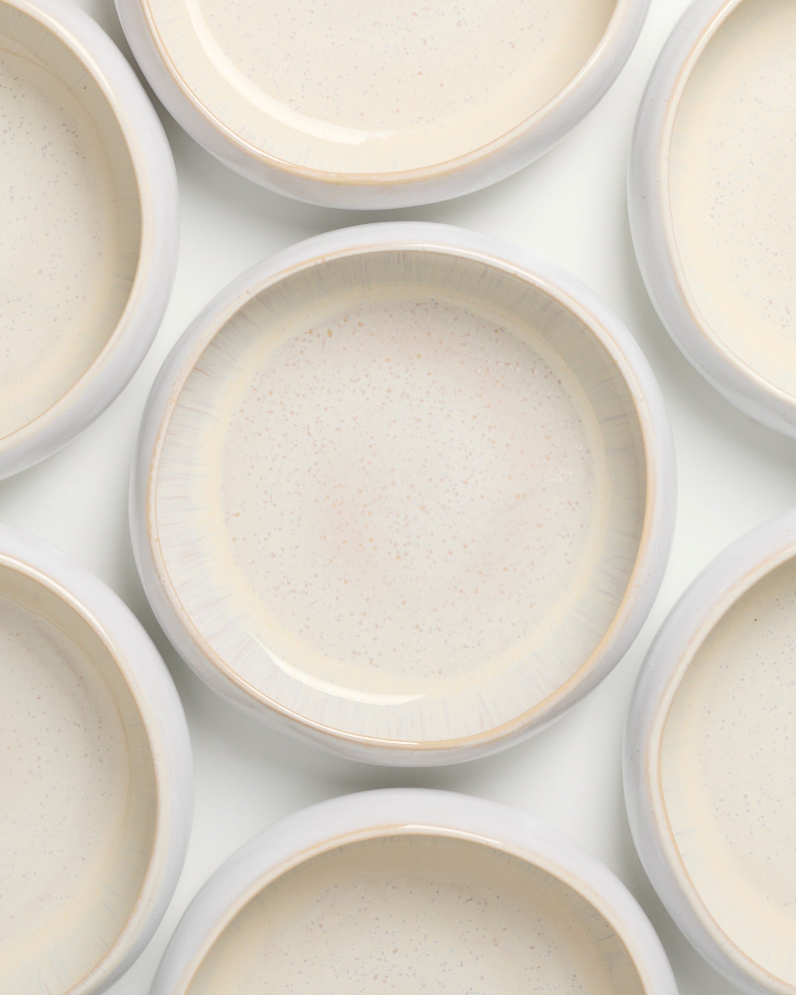 Mehrere beigefarbene Keramikteller mit hellen Rändern sind gleichmäßig angeordnet.