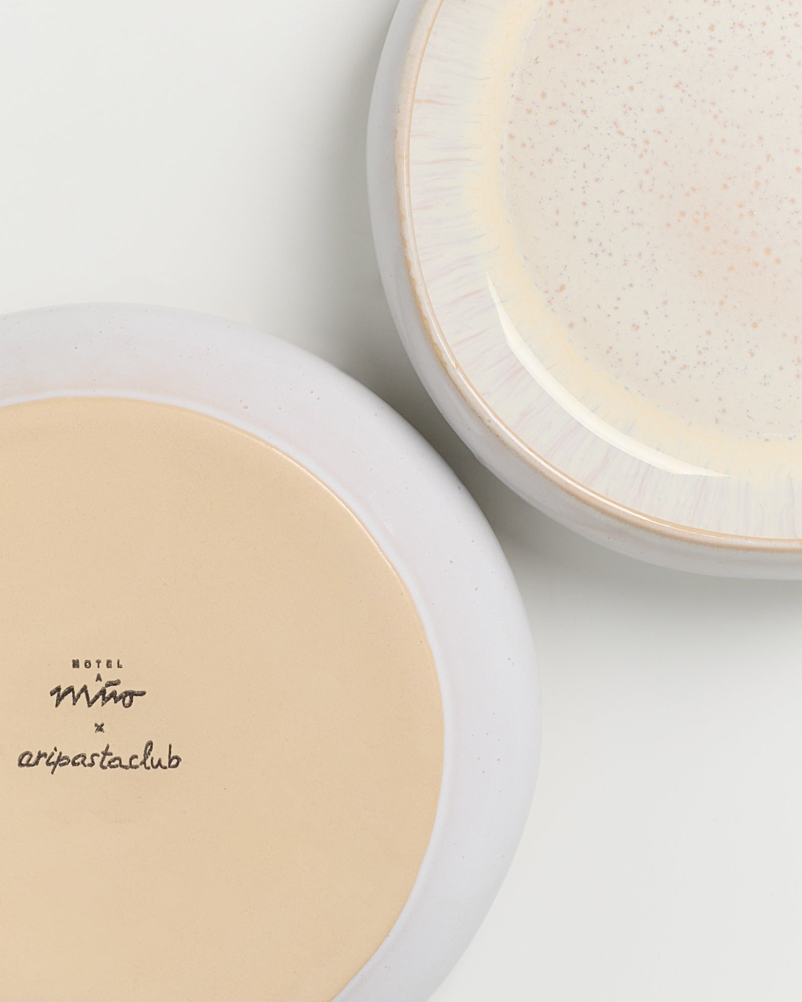 Zwei ineinandergreifende, runde Keramikteller, einer mit einer beigen Unterseite und schwarzem Text, der andere mit gesprenkelter Oberseite.