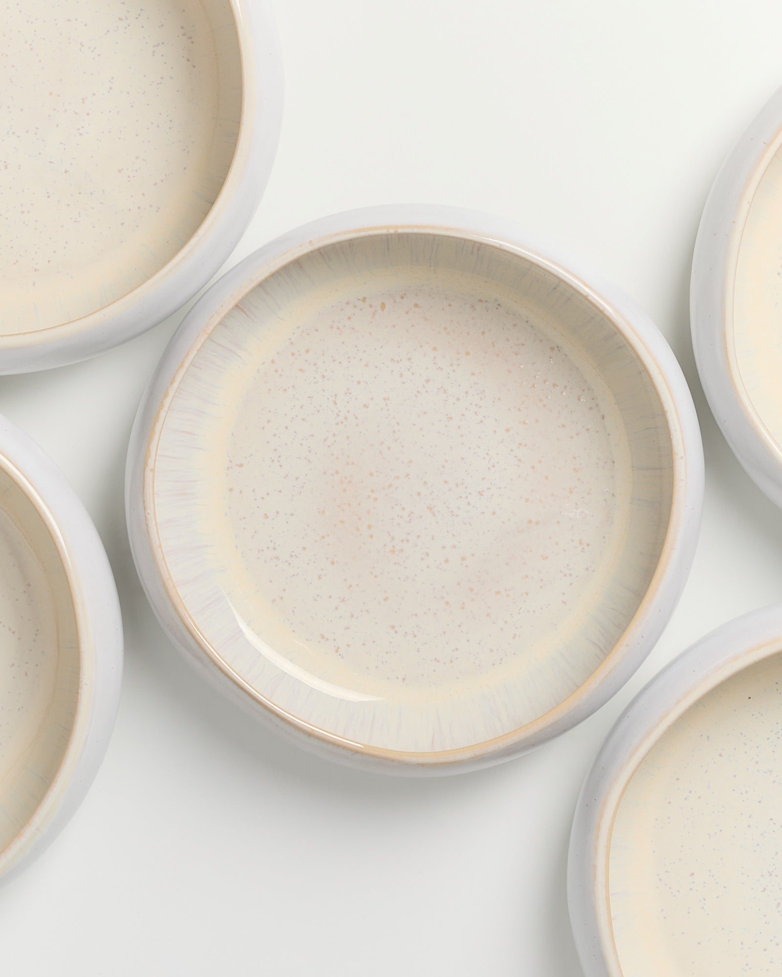 Mehrere cremefarbene, gesprenkelte Teller mit breitem Rand auf weißem Hintergrund.
