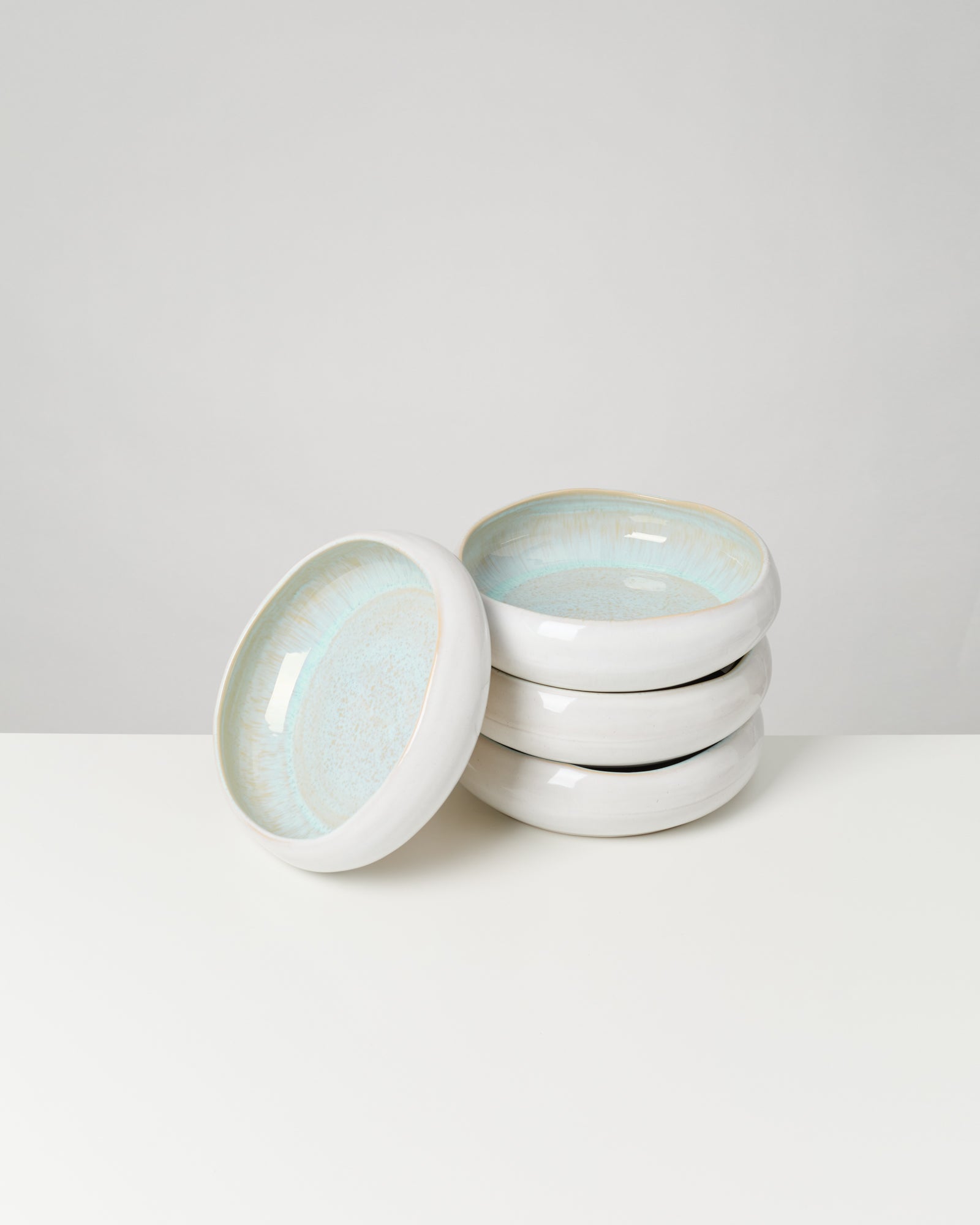 Ein Stapel von vier weißen Keramiktellern mit bläulichem Innenmuster auf weißem Hintergrund.