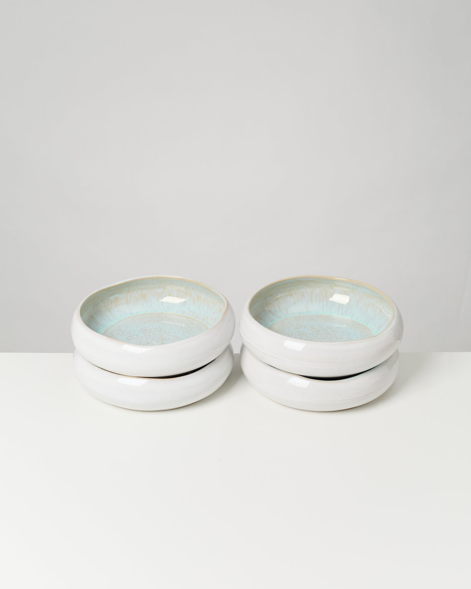 Vier gestapelte Keramikschalen mit hellblauer Glasur auf weißem Hintergrund.