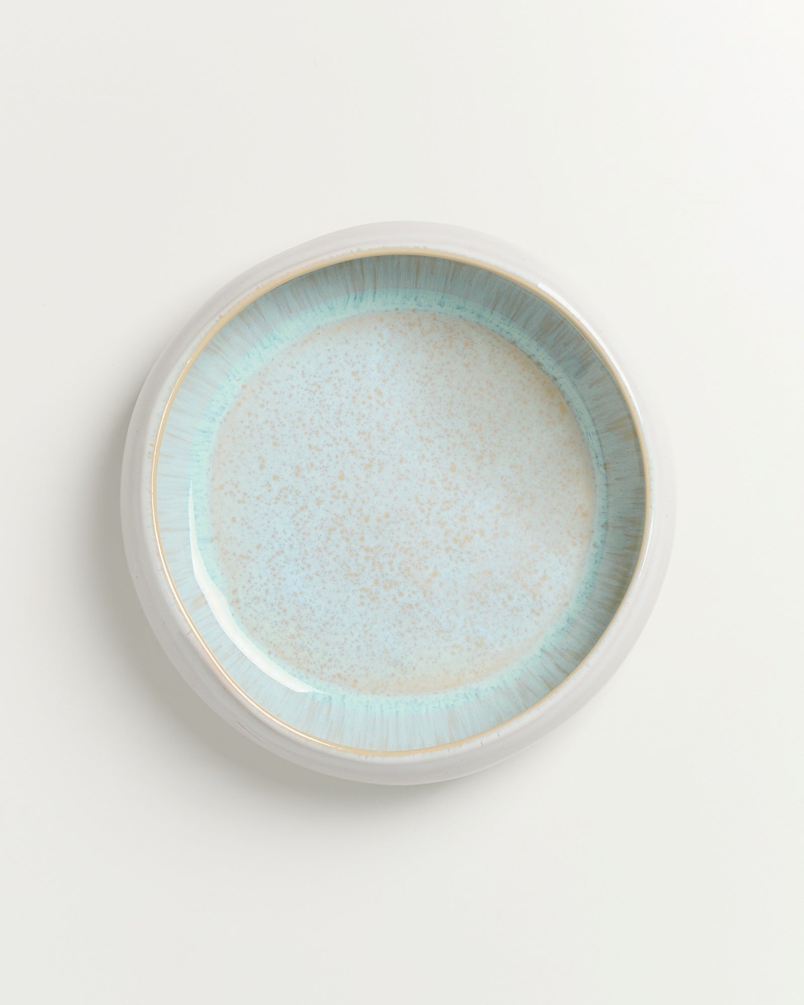 Runder, heller Keramikteller mit blauem Rand auf weißem Hintergrund.