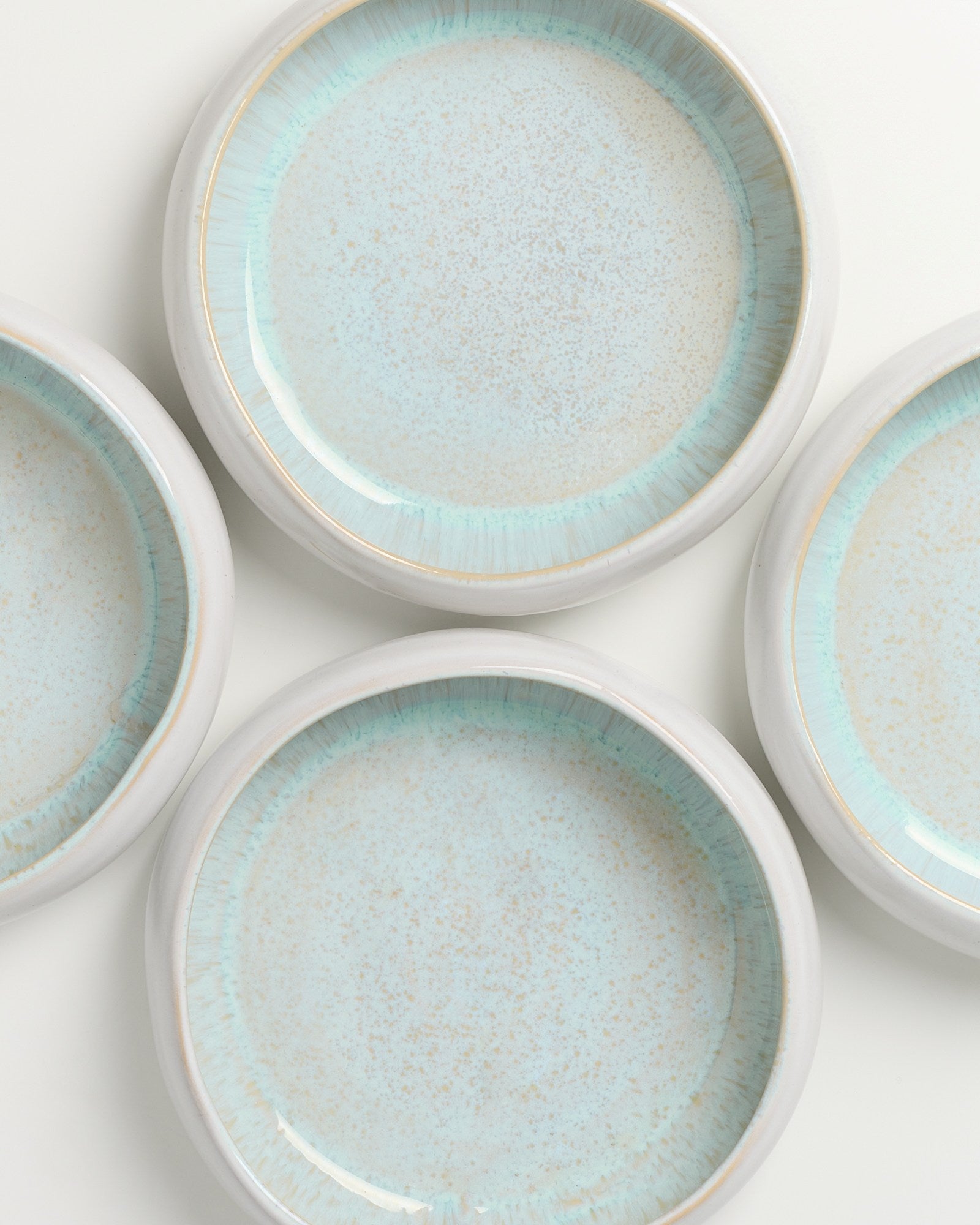 Vier runde, blau-gepunktete Keramikteller mit einem hellen Rand auf weißem Hintergrund.