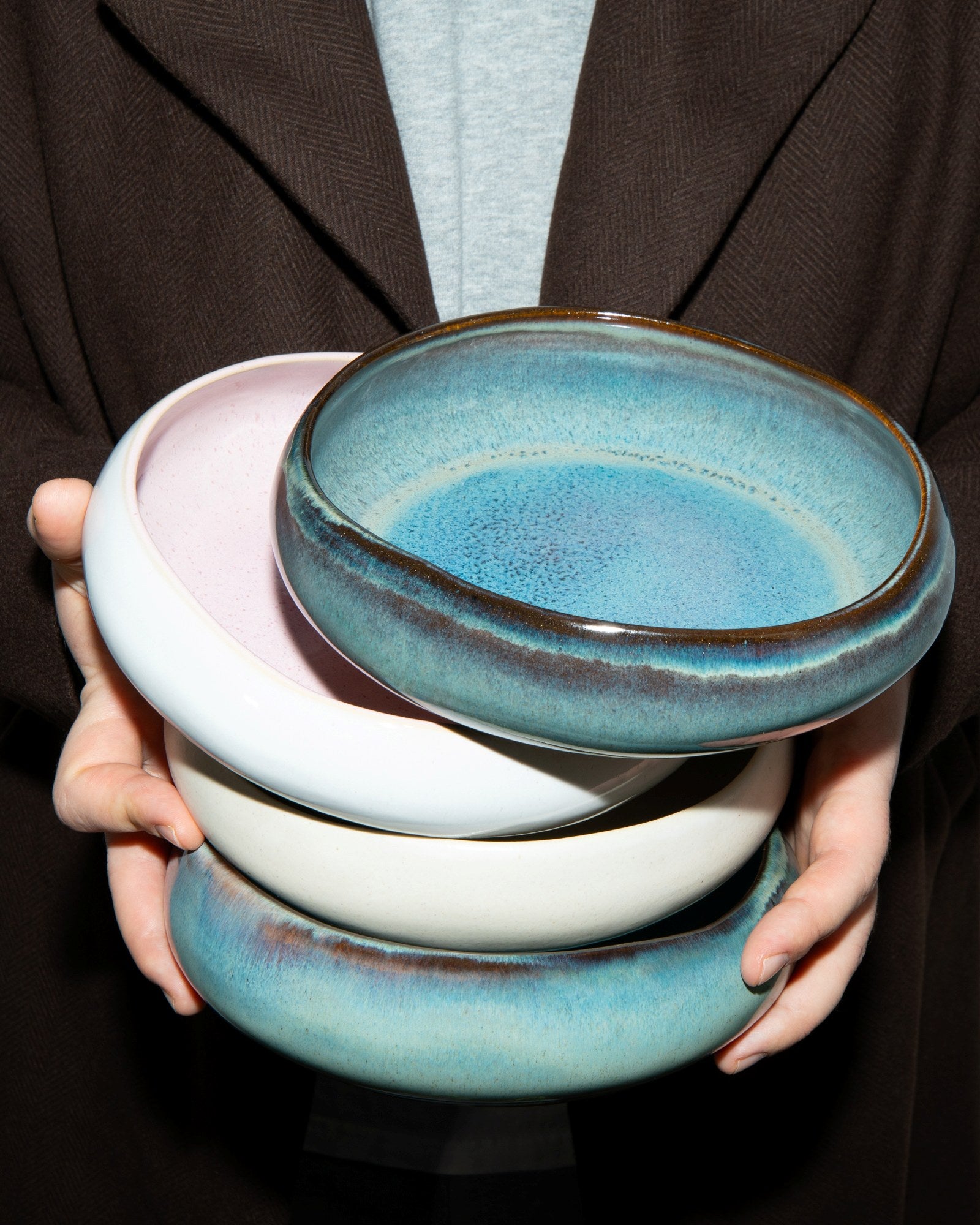 Person hält mehrere bunte Keramikschalen übereinander gestapelt.