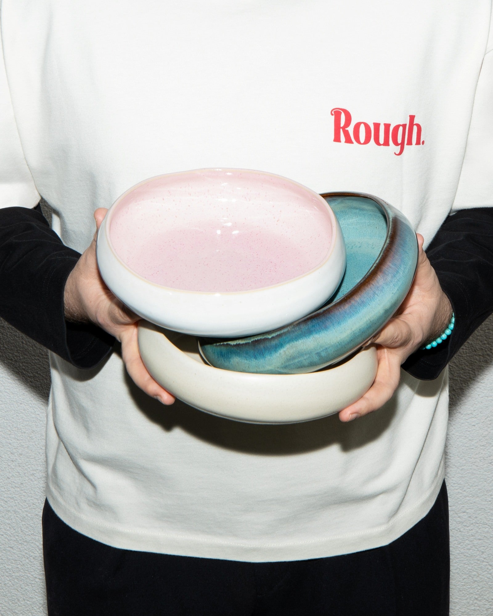 Person hält drei stapelbare Schalen in Pastellfarben; auf dem Shirt steht "Rough".